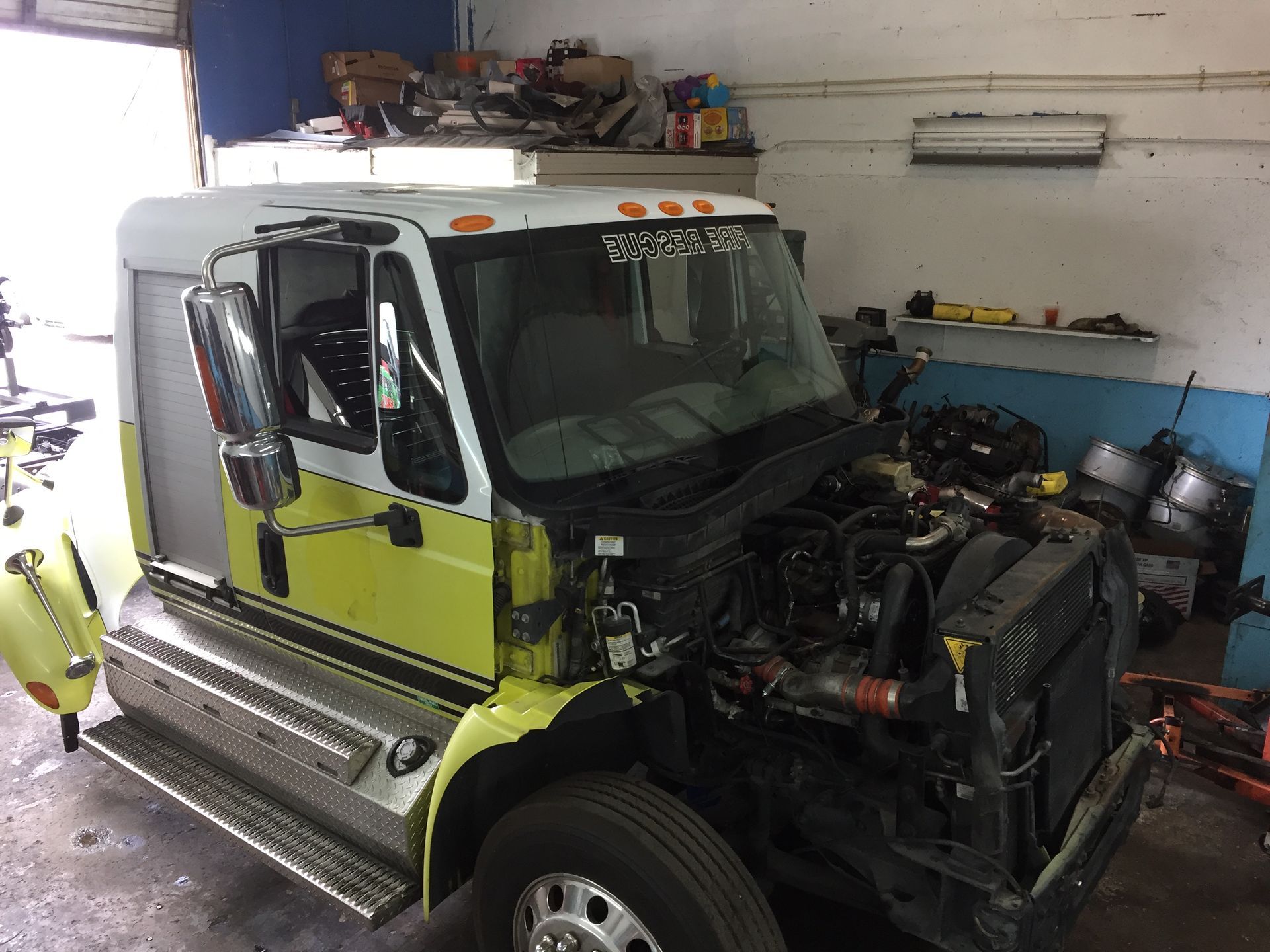 A yellow and white truck is sitting in a garage with its hood up.