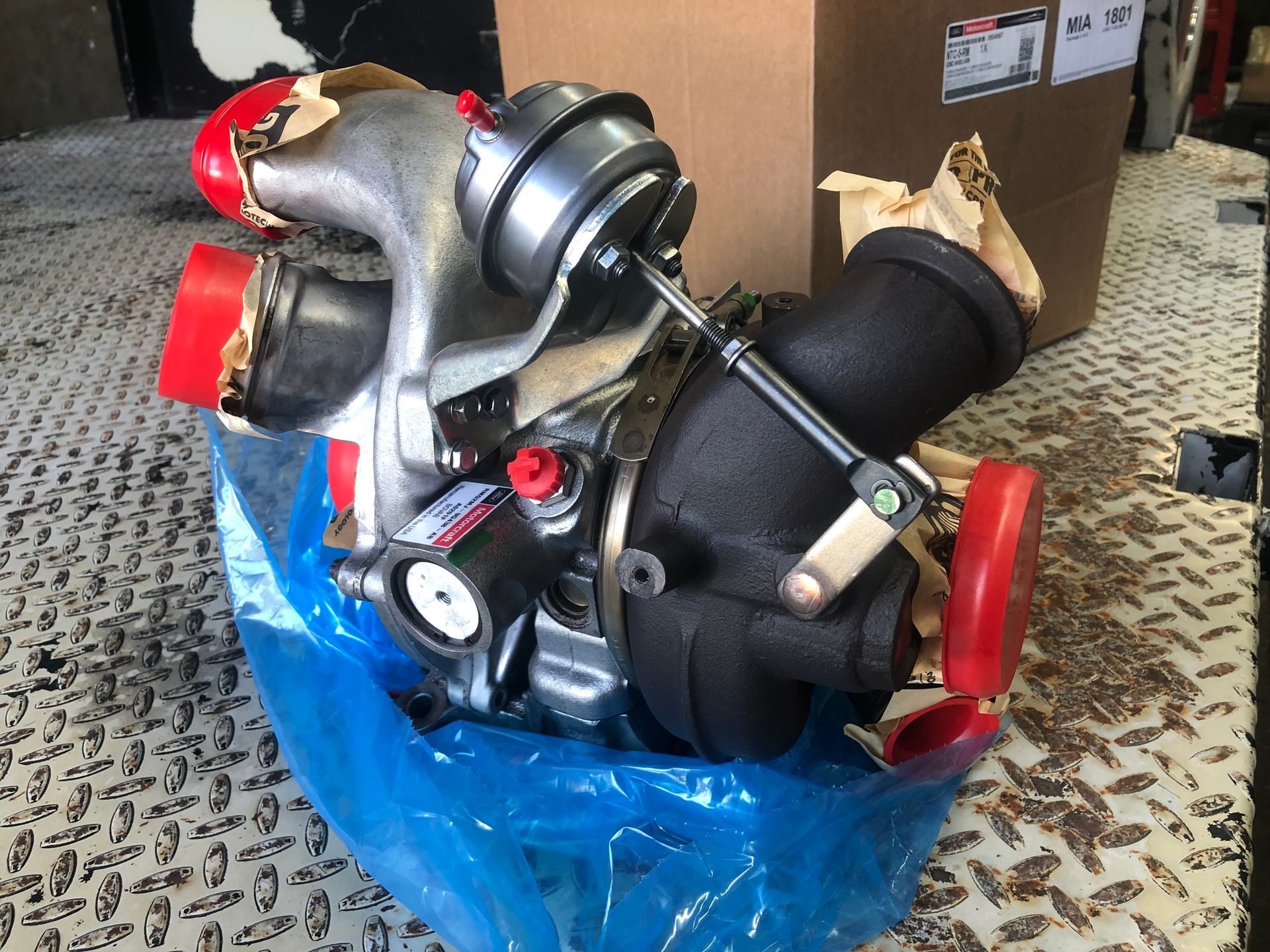 A turbocharger is wrapped in plastic and sitting on a metal surface