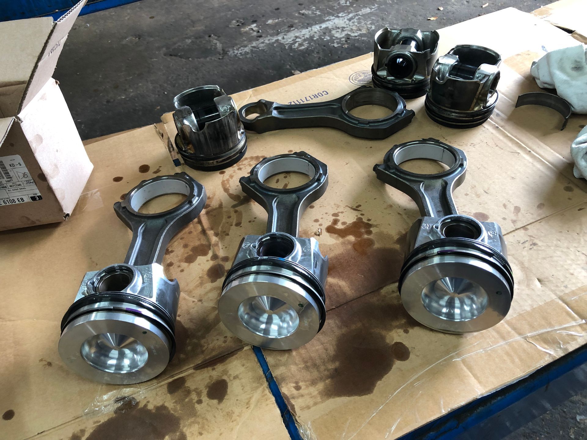 A group of pistons and connecting rods are sitting on a piece of cardboard.