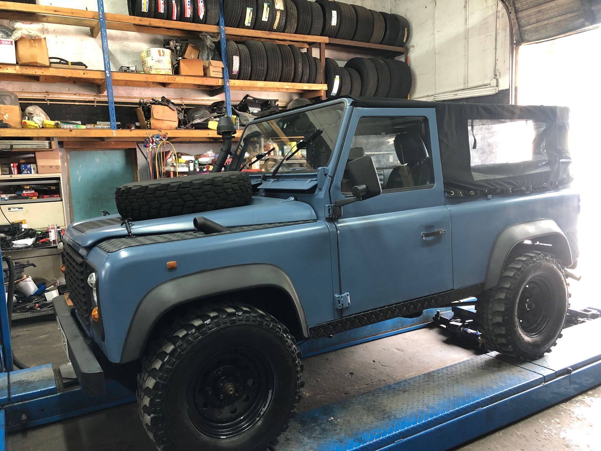 A blue land rover defender is sitting on a lift in a garage.