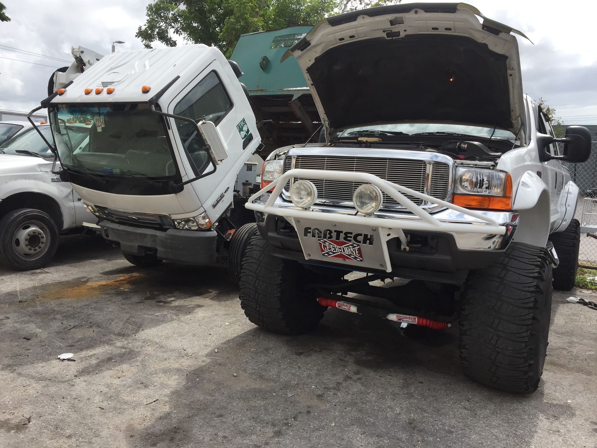 A truck with the hood up is parked next to another truck