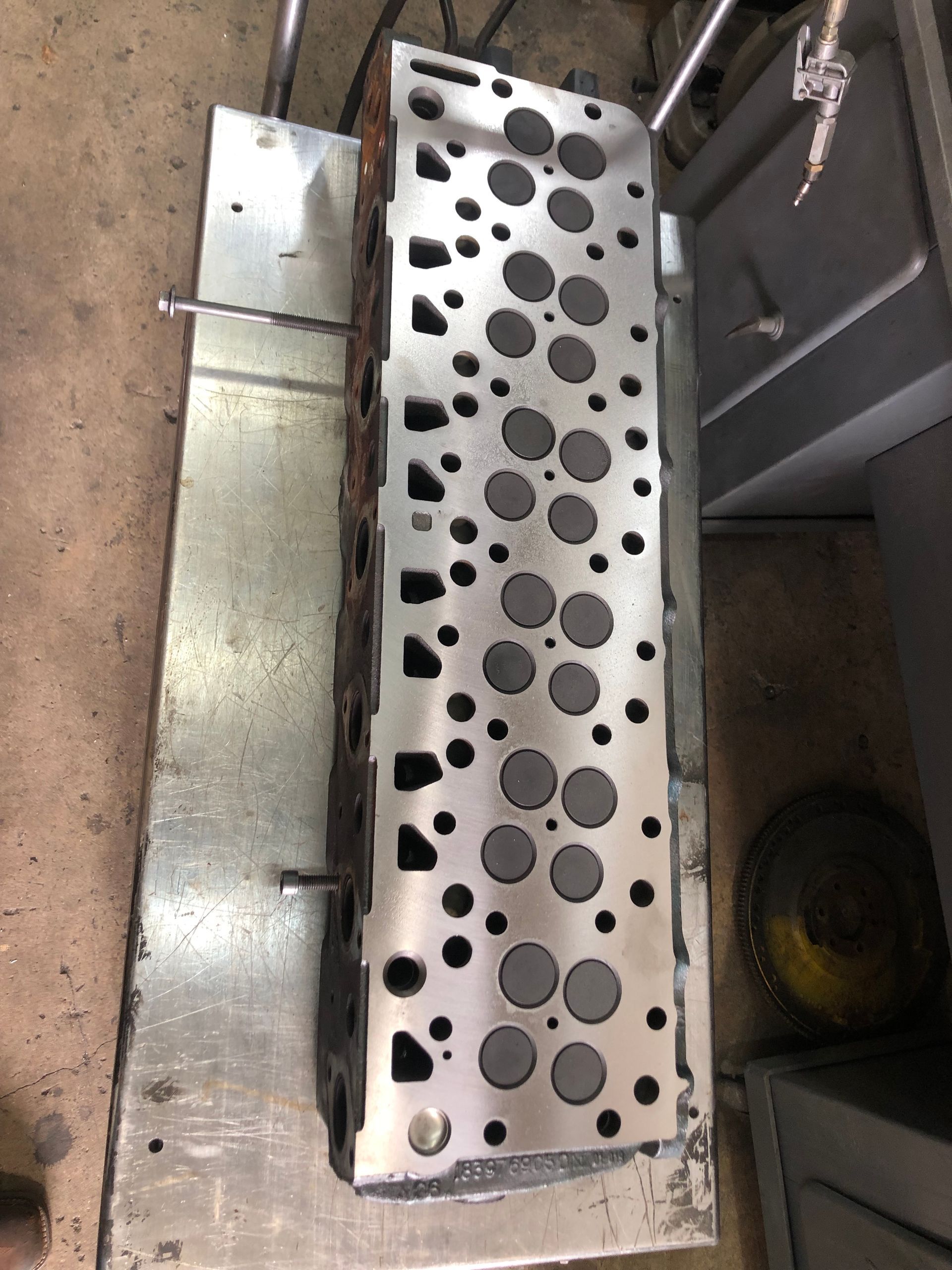 A metal cylinder head with holes in it is sitting on a metal table.