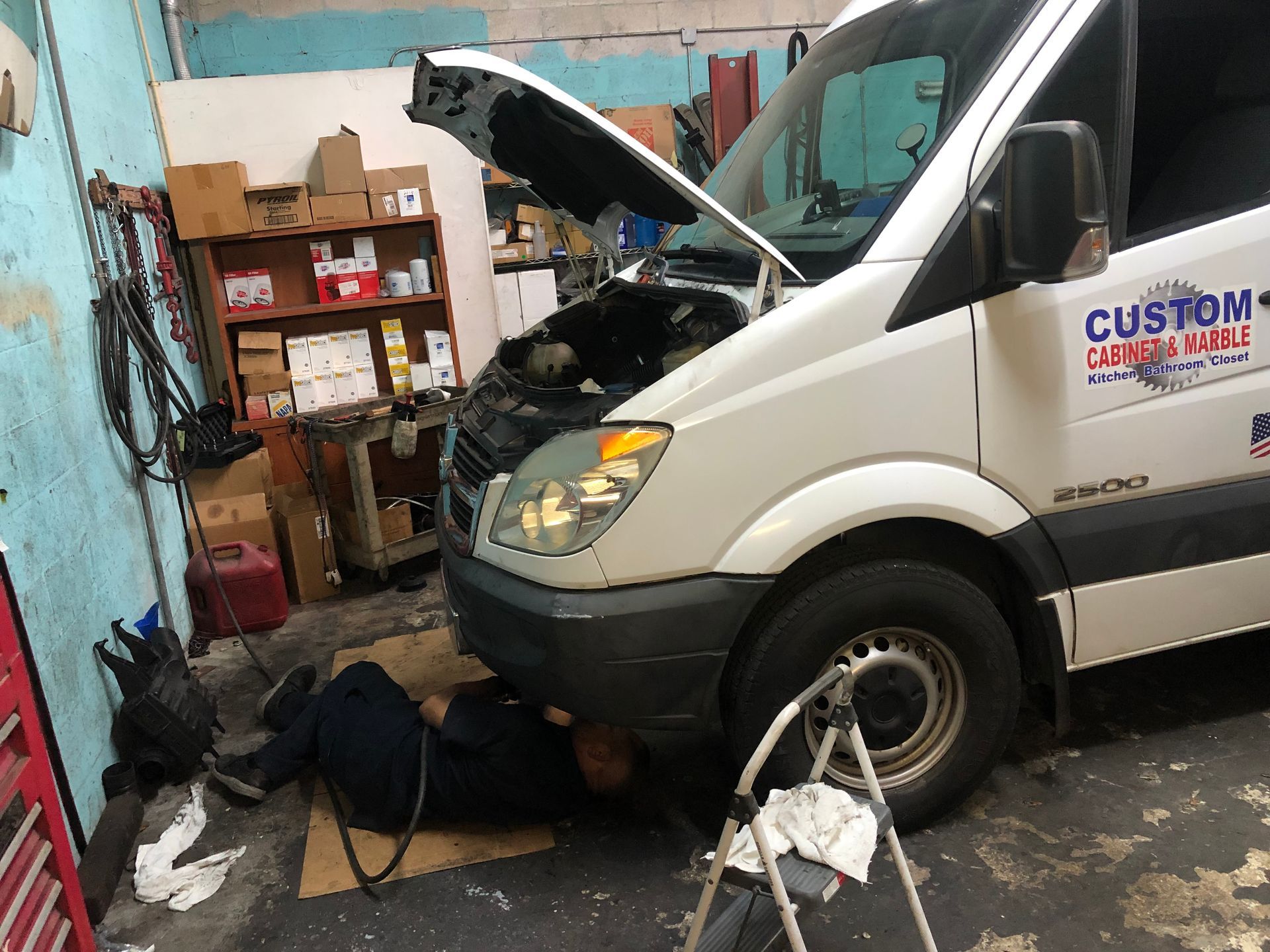 A man is working under the hood of a white van in a garage.