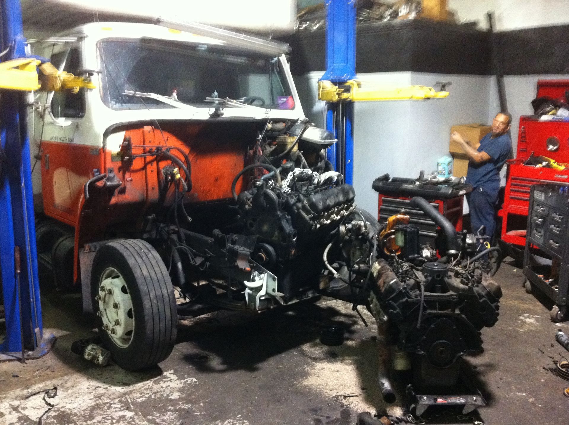 A truck is being worked on in a garage with the engine removed