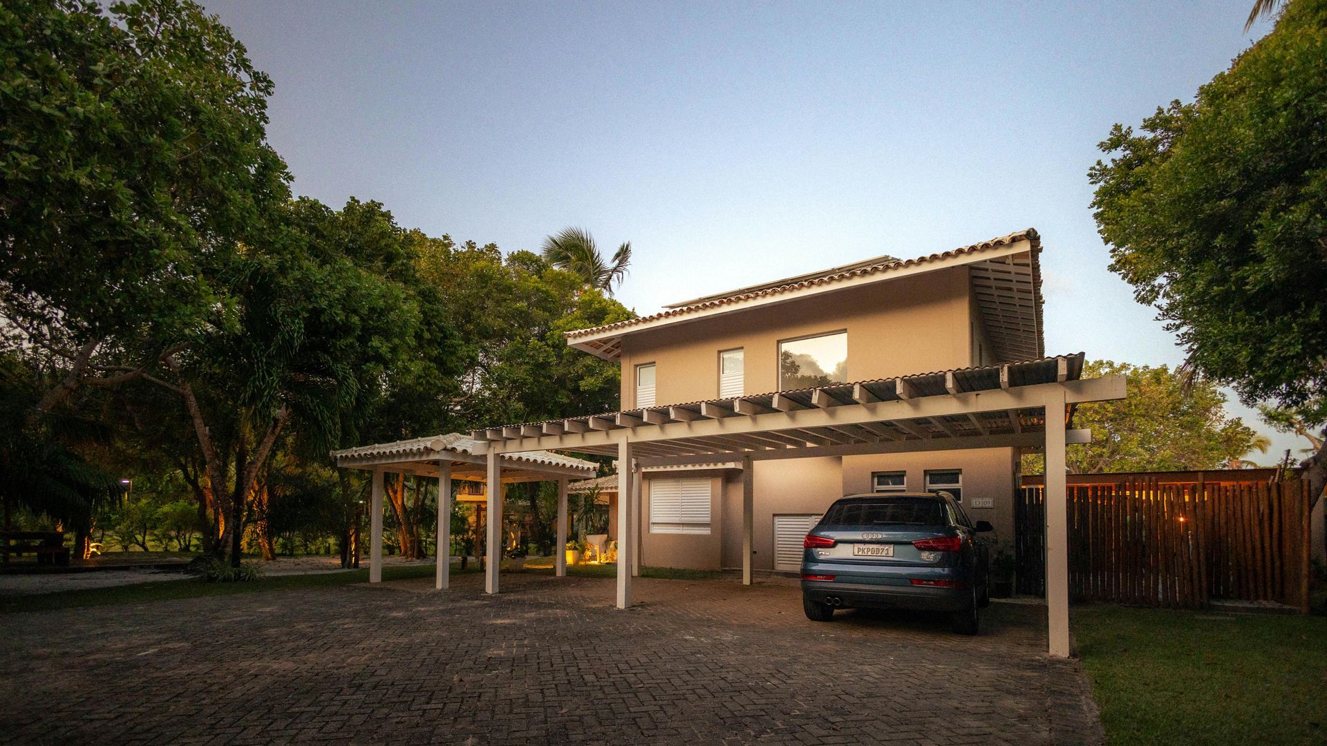 Beige two-story house with a pergola-covered carport; a gray car is parked under it.