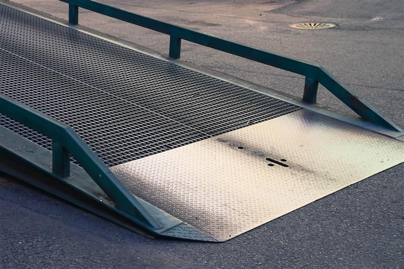 Metal ramp with mesh surface and green handrails on asphalt.