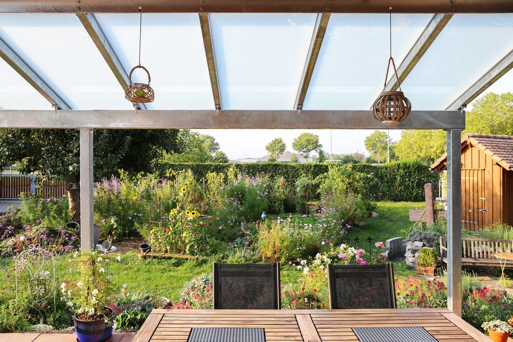 A garden with flowers, grass, and a wooden table under a transparent roof.