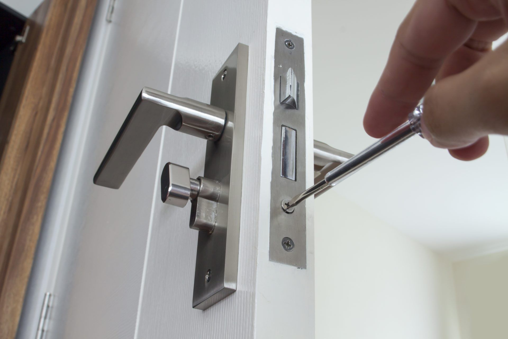 A person is fixing a door lock with a screwdriver.