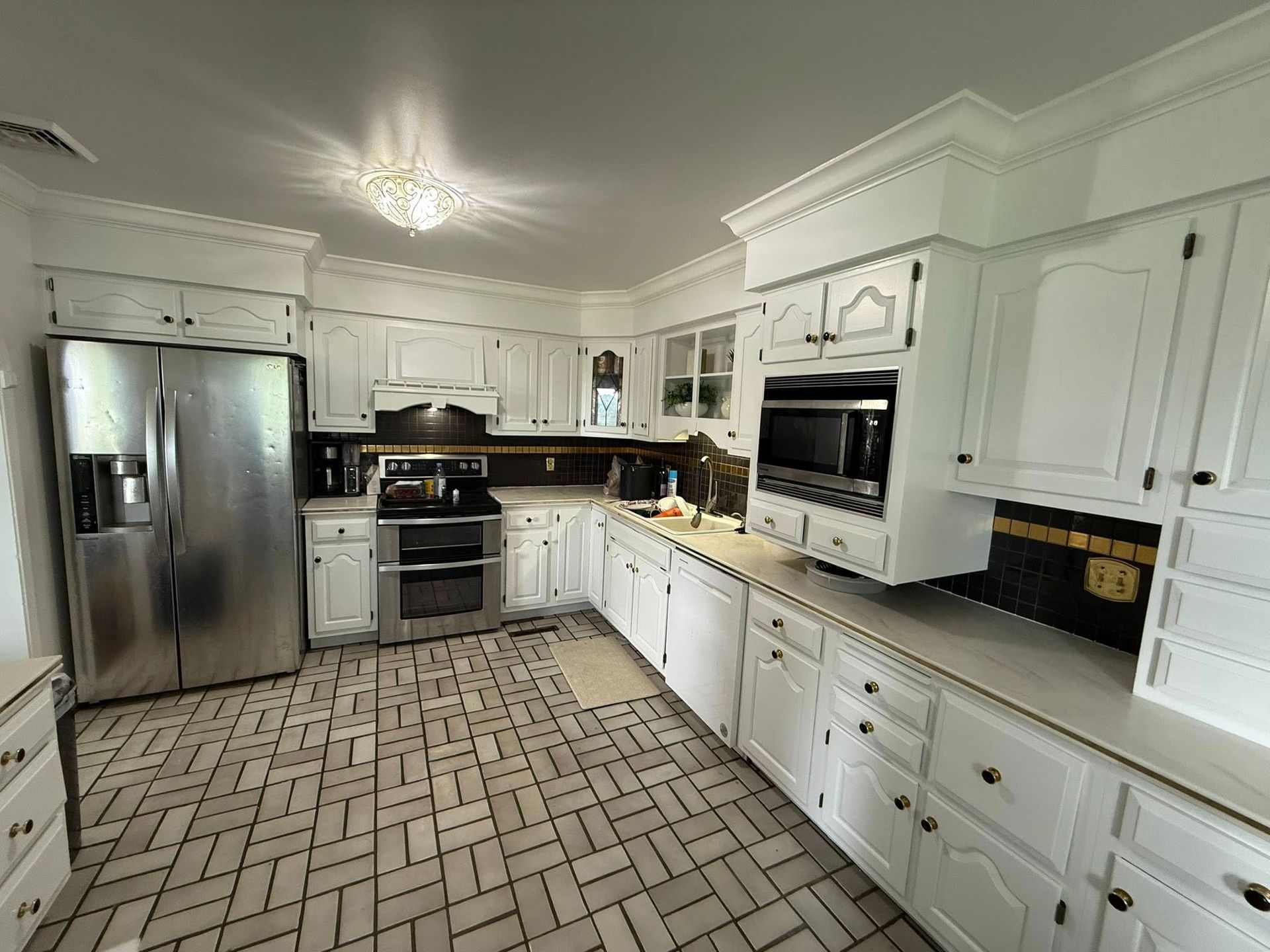 A kitchen with white cabinets, stainless steel appliances, and a gray patterned tiled floor.