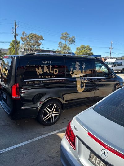 A black van is parked next to a silver car in a parking lot — Signworld In Mitchell, ACT