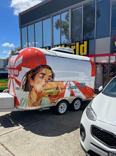 A Food Truck With a Picture of a Woman Eating a Hamburger is Parked in Front of a Building — Signworld In Mitchell, ACT