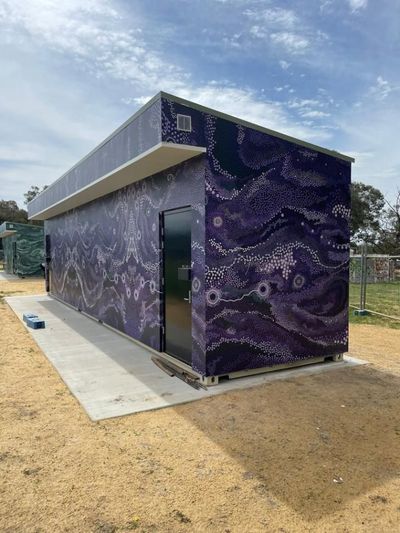 A Purple Building With a Painting on the Side is Sitting on Top of a Dirt Field — Signworld In Mitchell, ACT