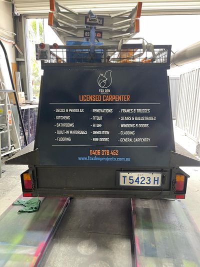 A black trailer with a sign on the back is parked in a garage — Signworld In Mitchell, ACT