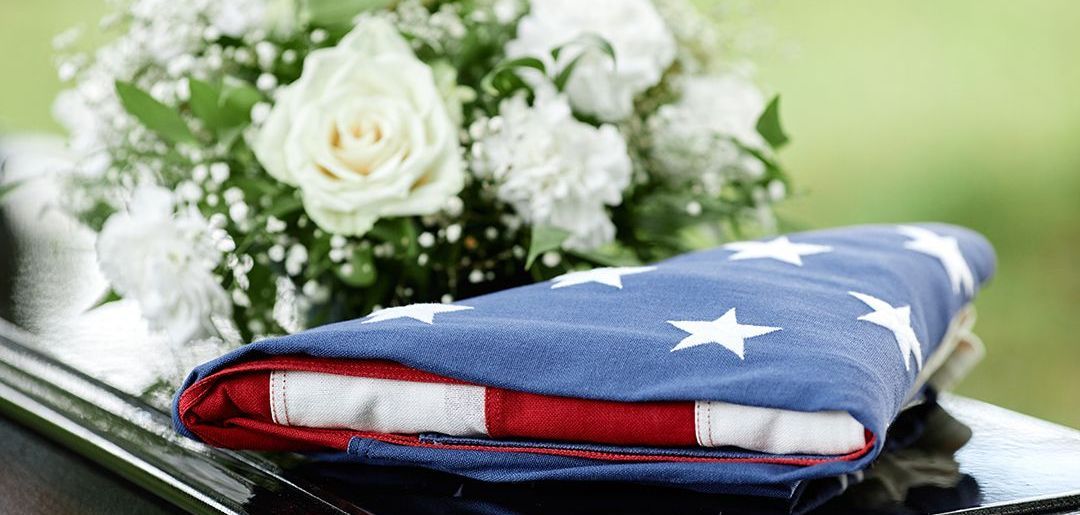 A woman is holding an american flag and a rose at a funeral.