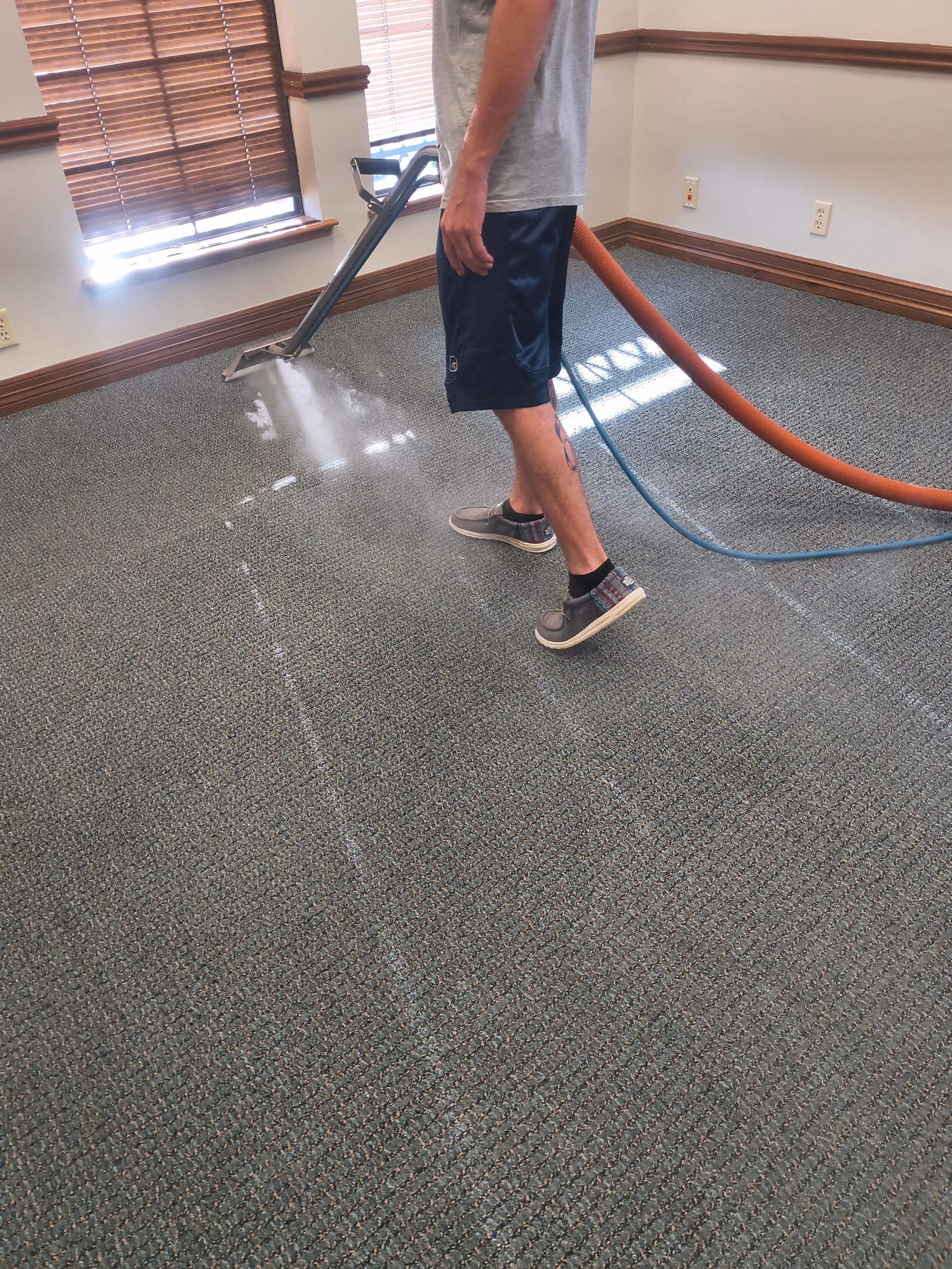 Person cleaning a mottled gray carpet with a carpet cleaner in a room.
