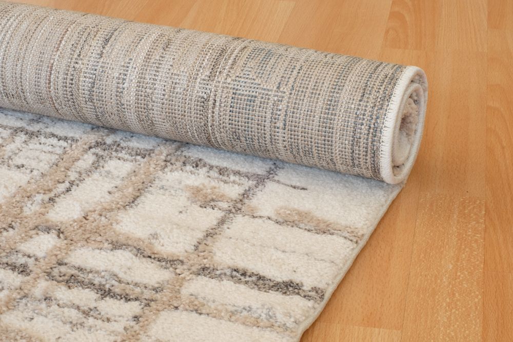 Rolled-up beige and tan patterned rug on a wooden floor, partially unrolled showing the design.