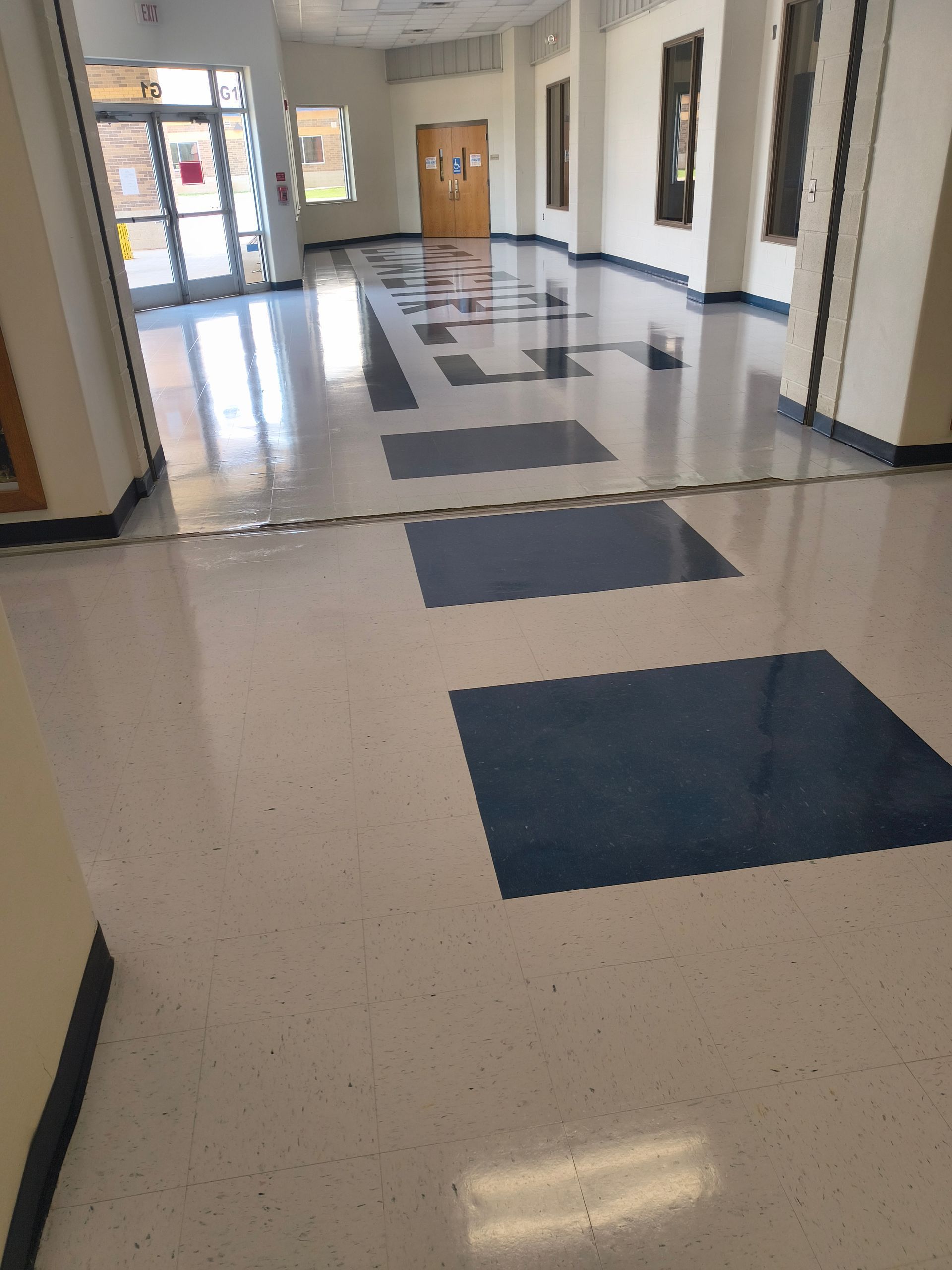Hallway with white and blue tiled floor, leading to a door at the end. Sunlight streams in from a side window.