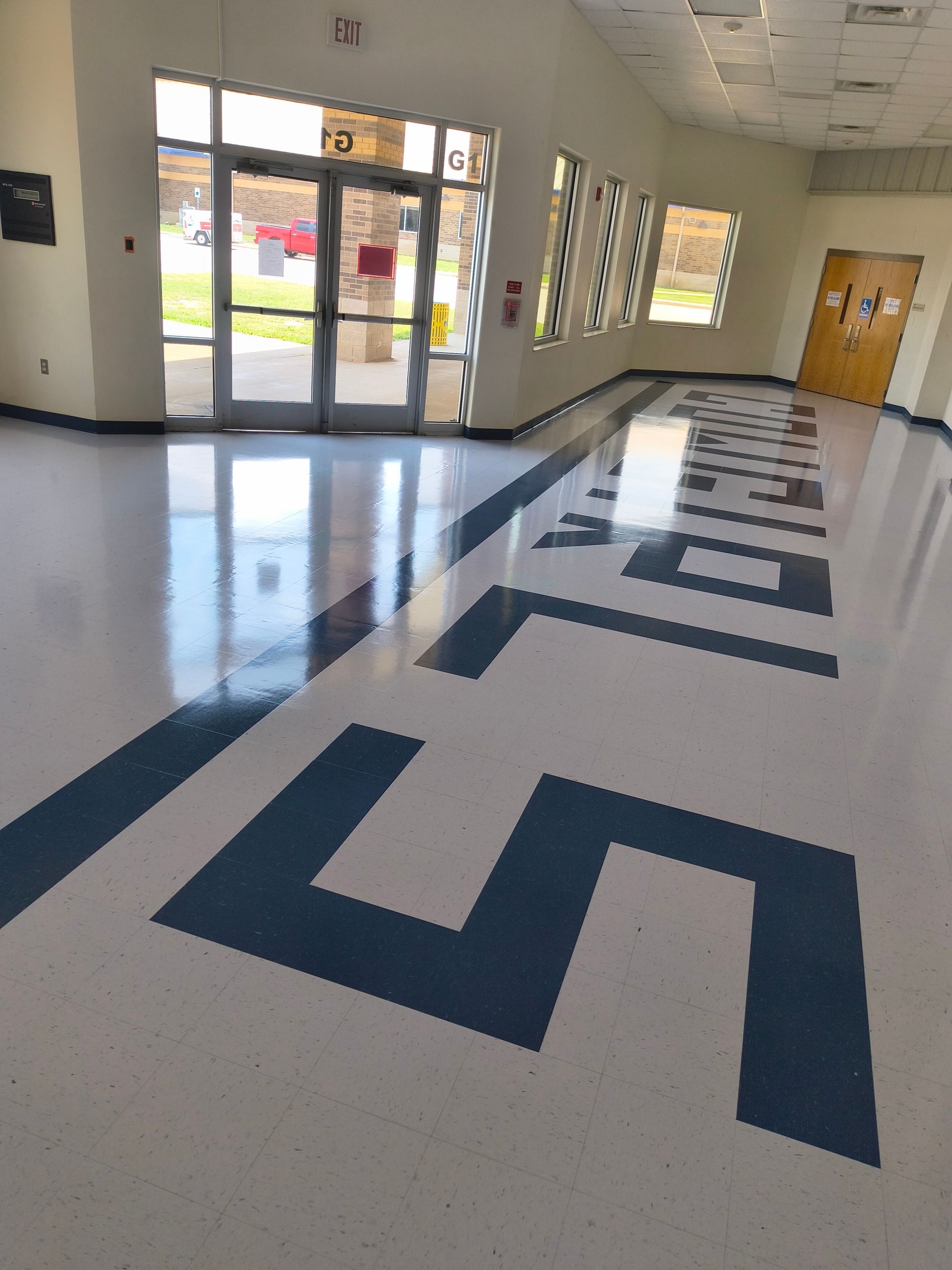 Hallway with a blue and white patterned floor, leading to an entryway with glass doors.