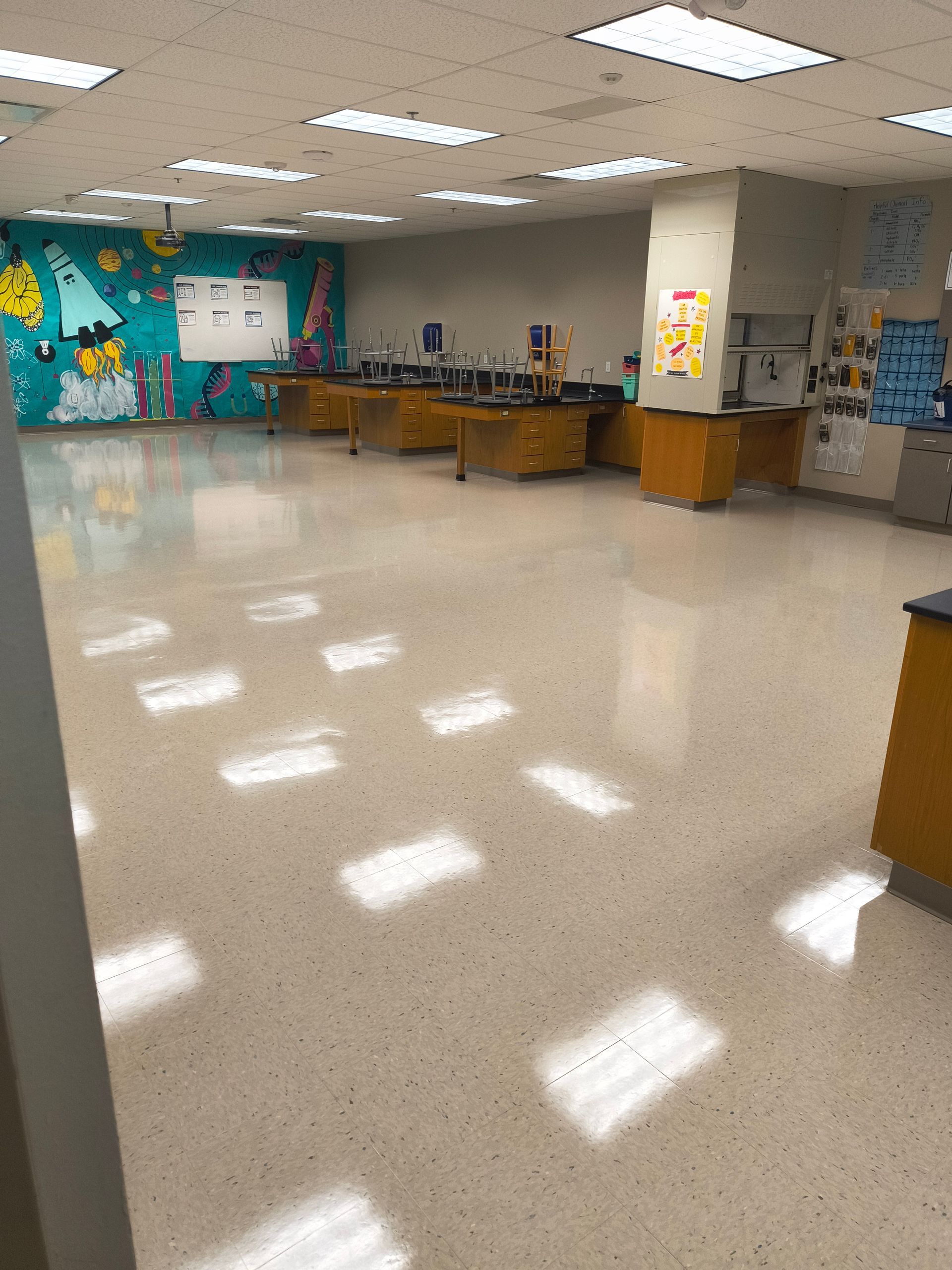 Empty science classroom with lab tables, whiteboards, and colorful wall art. Brightly lit with shiny floor.