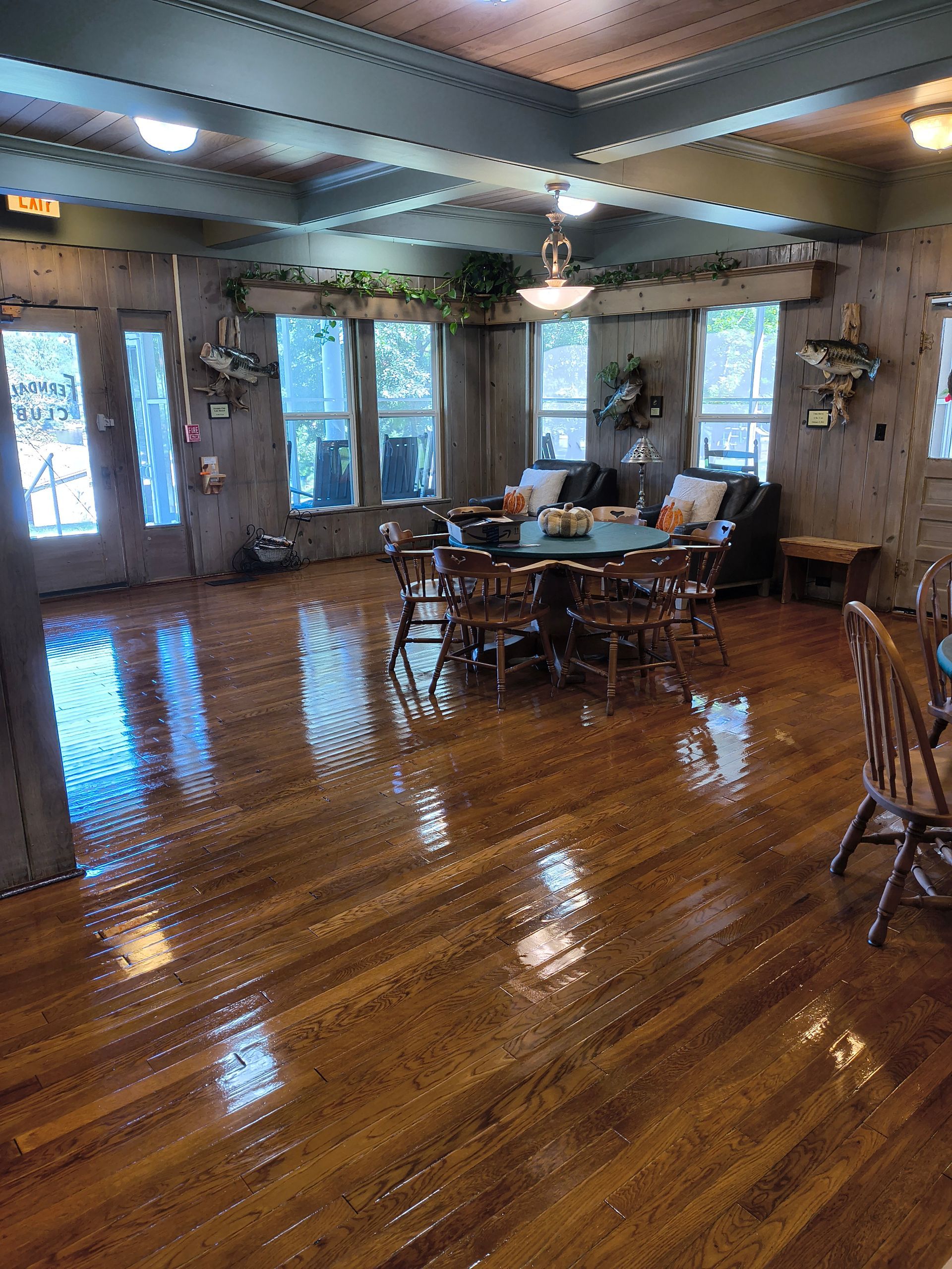 Interior of a room with shiny wood floors, tables, chairs, and windows with outdoor views.