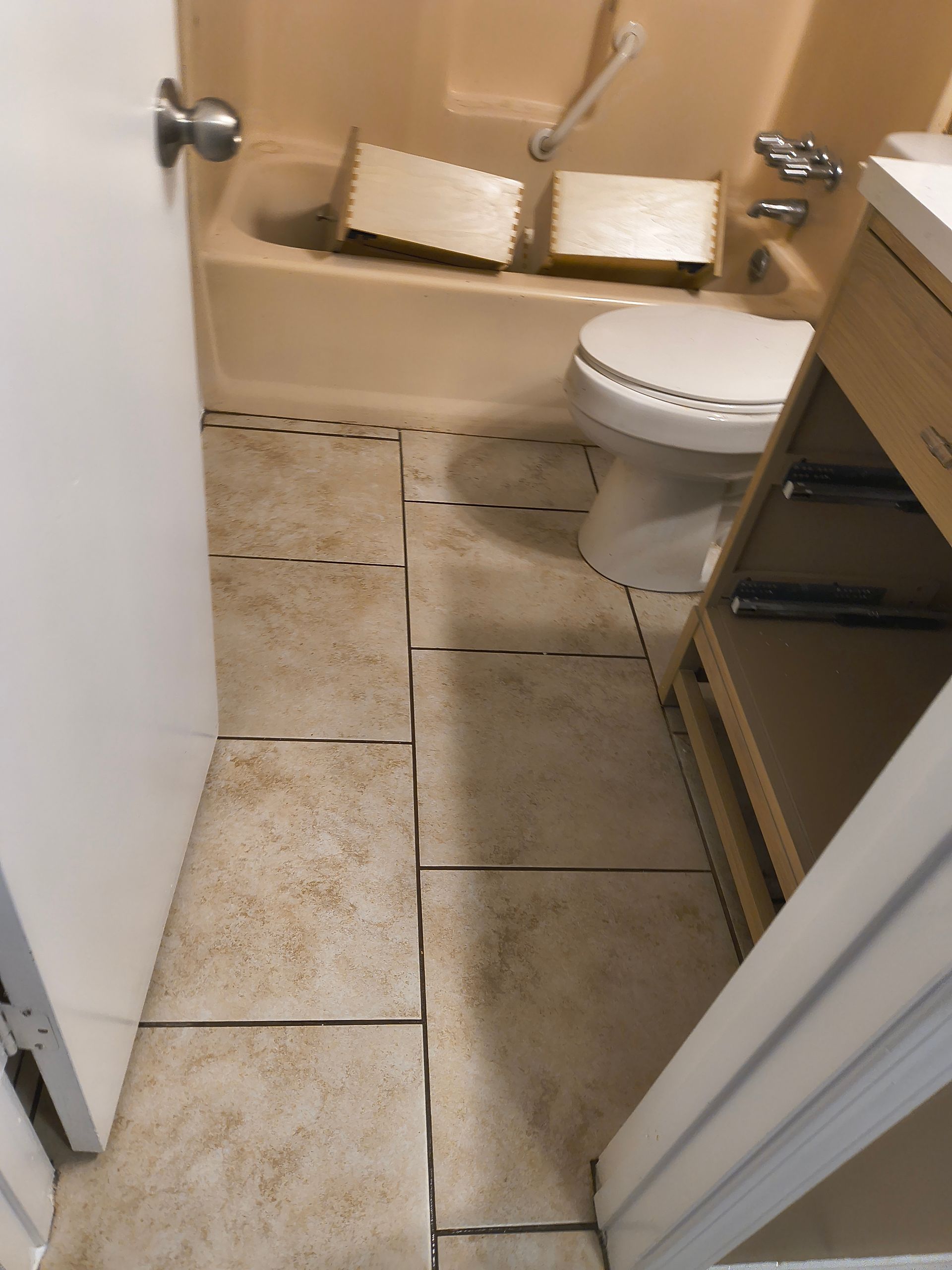 Bathroom with tile flooring and bathtub. Toilet and cabinet are present. Tile installation is incomplete.