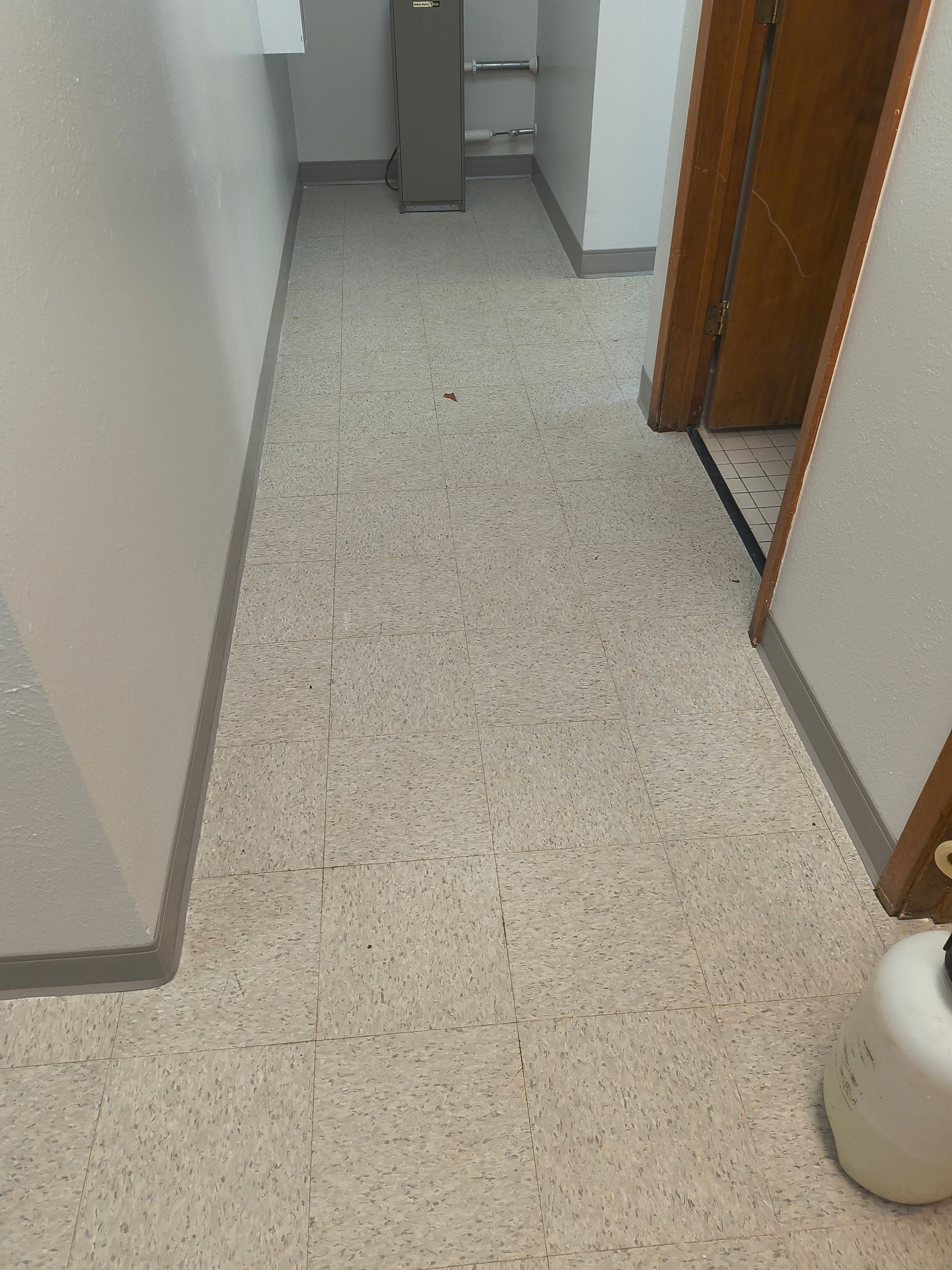 Hallway with speckled floor, white walls, and a closed wooden door.