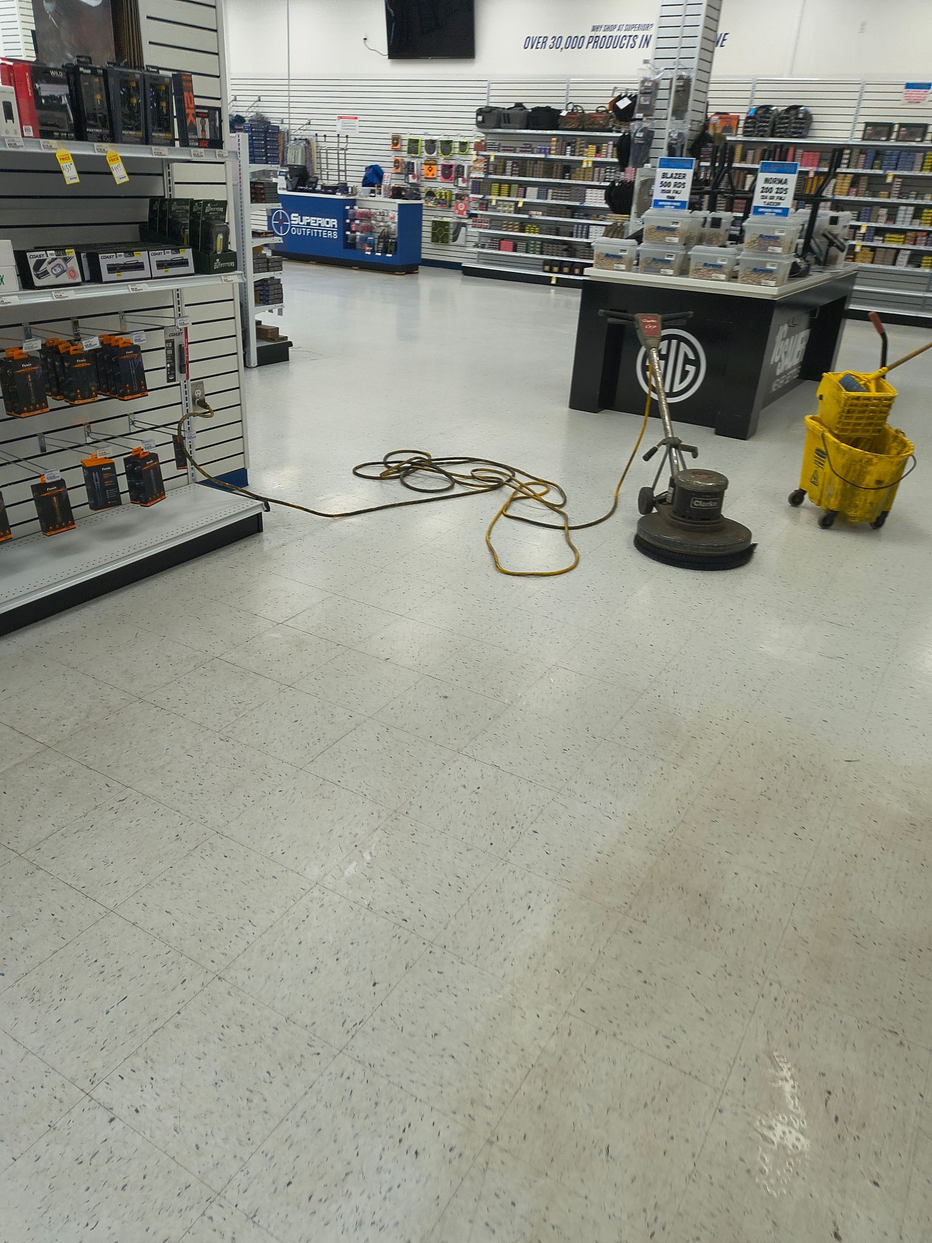 Floor cleaning machine in a retail store, yellow bucket, electrical cord, white floor, shelves of merchandise.