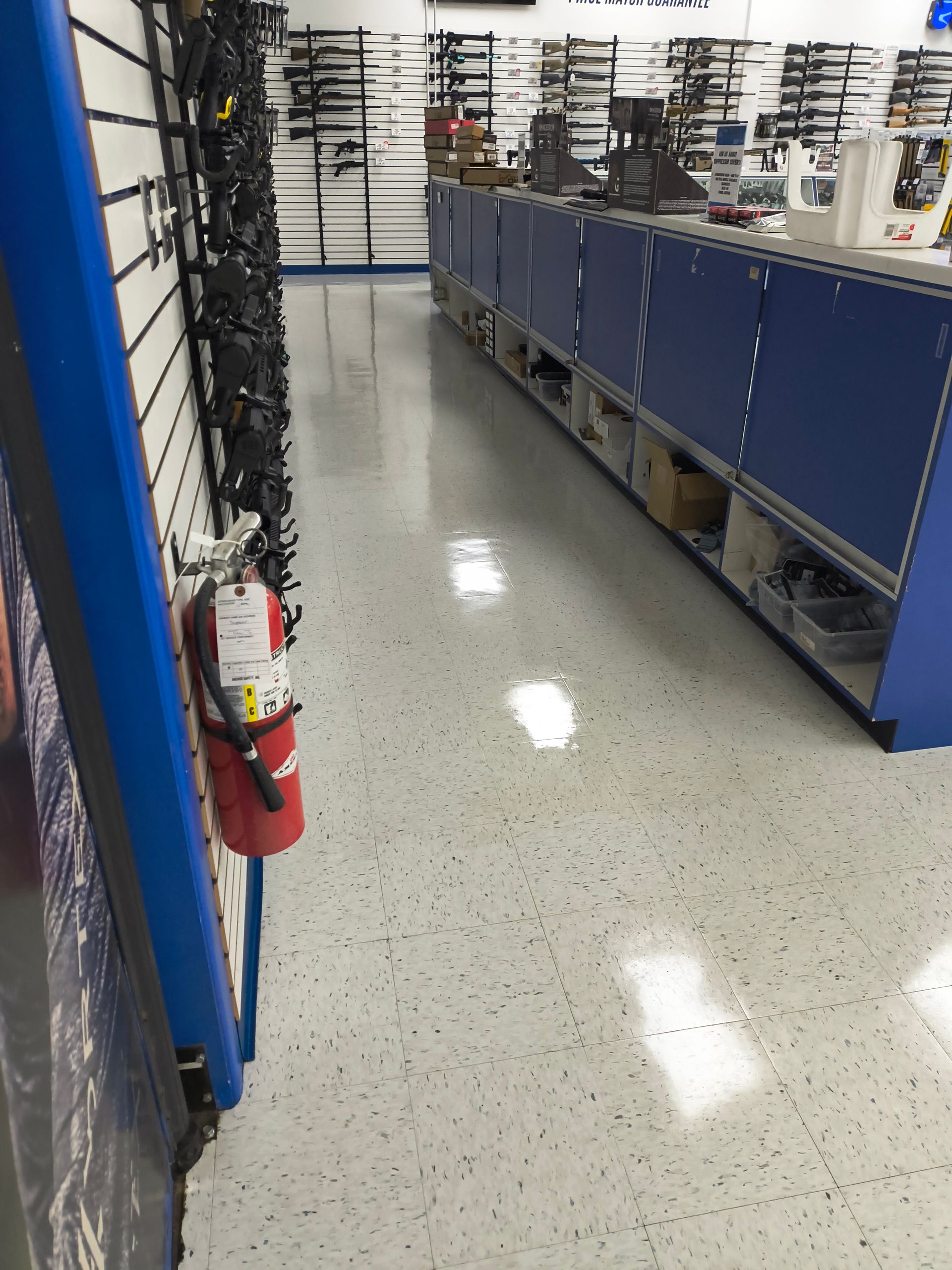 Fire extinguisher and merchandise display inside a store. White and gray speckled floor, blue wall.