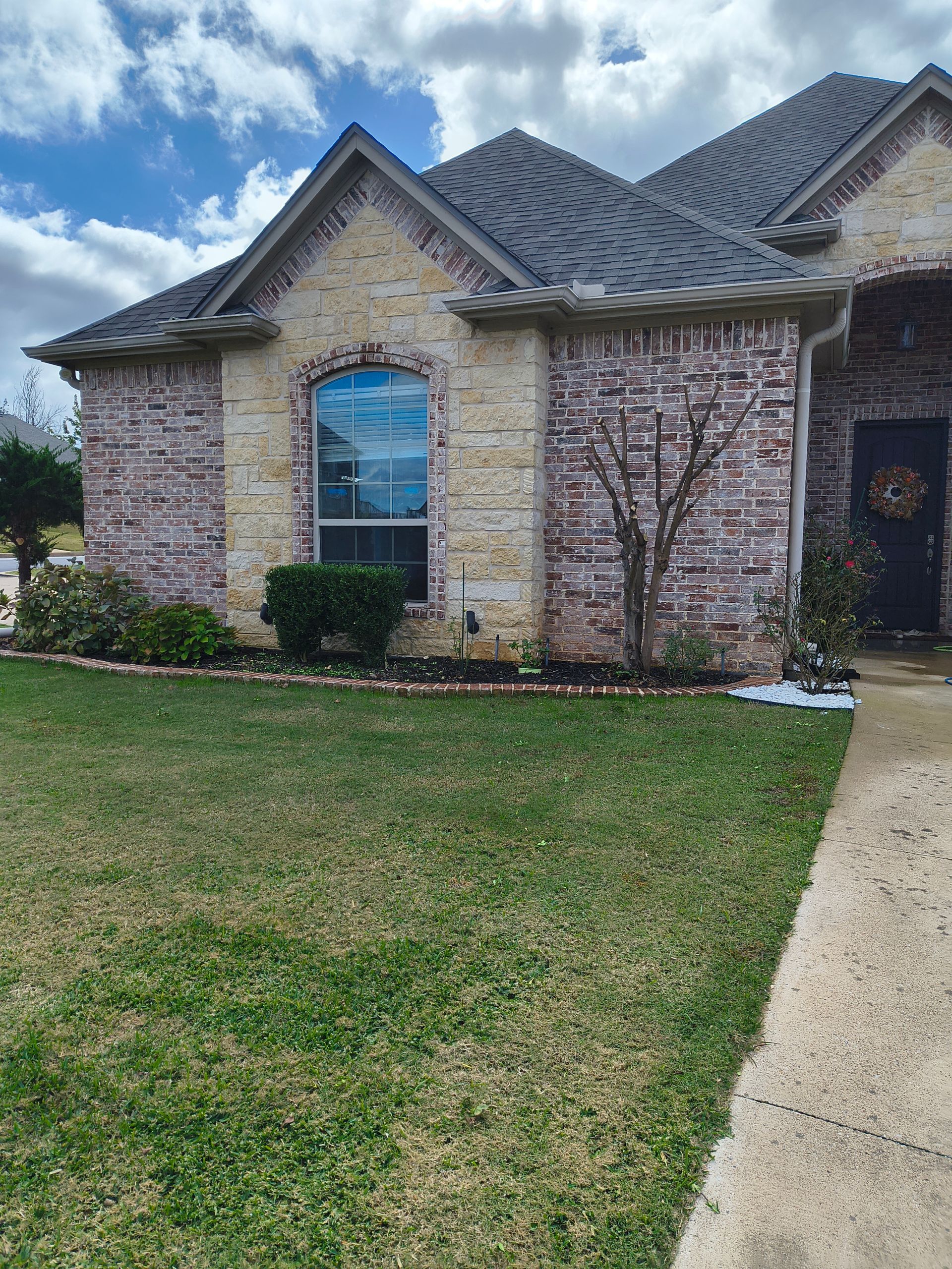 Brick home with dark roof, arched window, and green lawn under a cloudy sky.