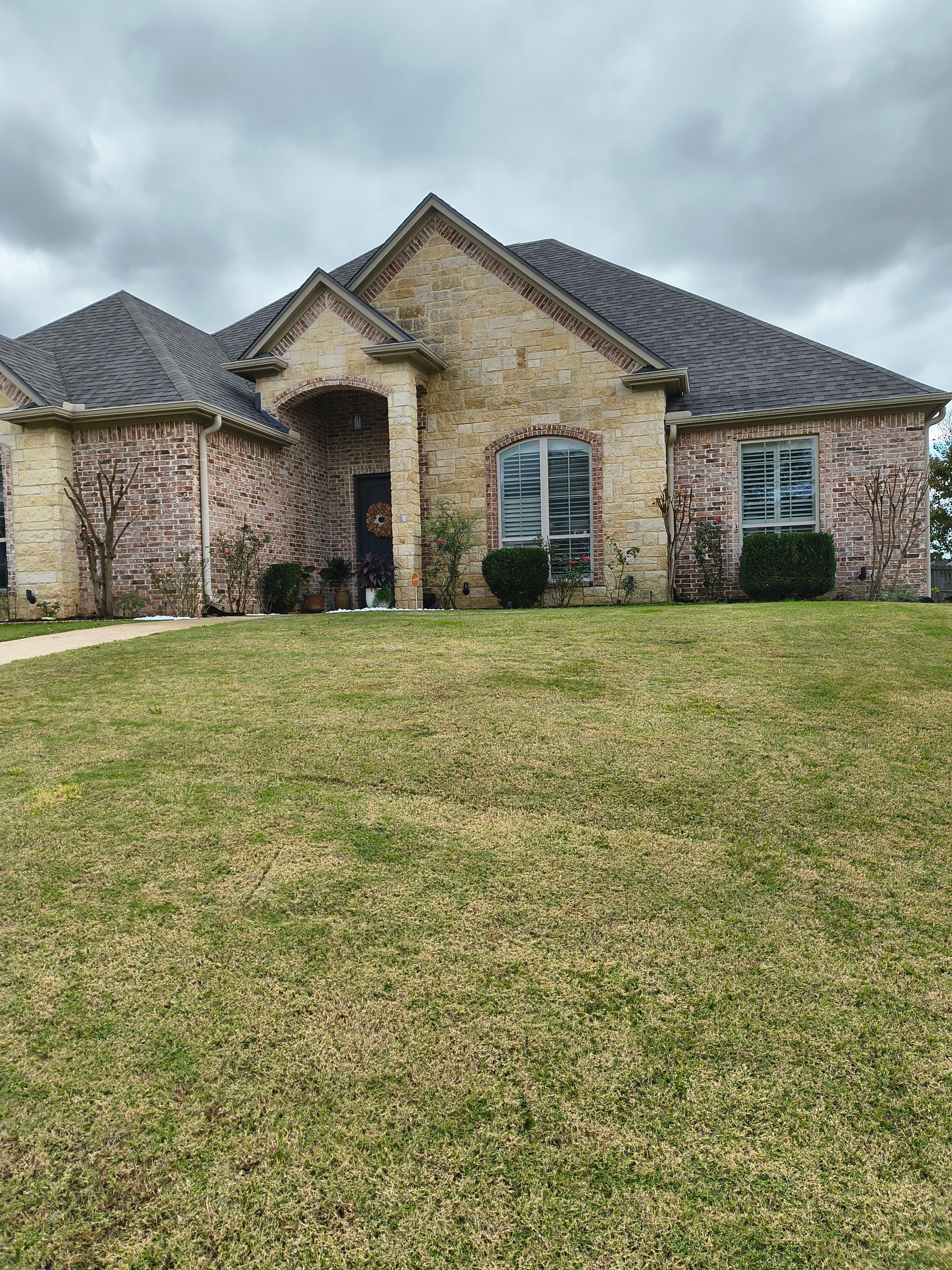 Brick house with arched windows under a cloudy sky, on a grassy hill.