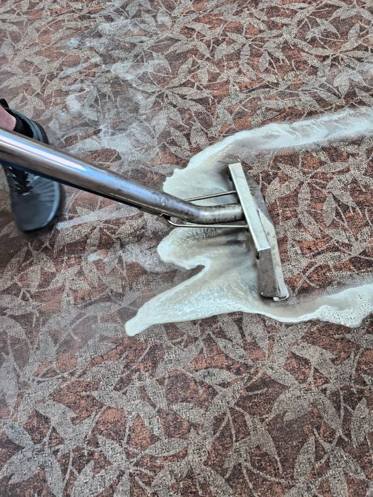A person cleaning a brown and tan patterned floor with a floor cleaning machine.