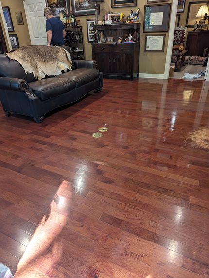 Person mopping a wooden floor with a white mop. Blue jeans, striped socks, and a light shirt are visible.