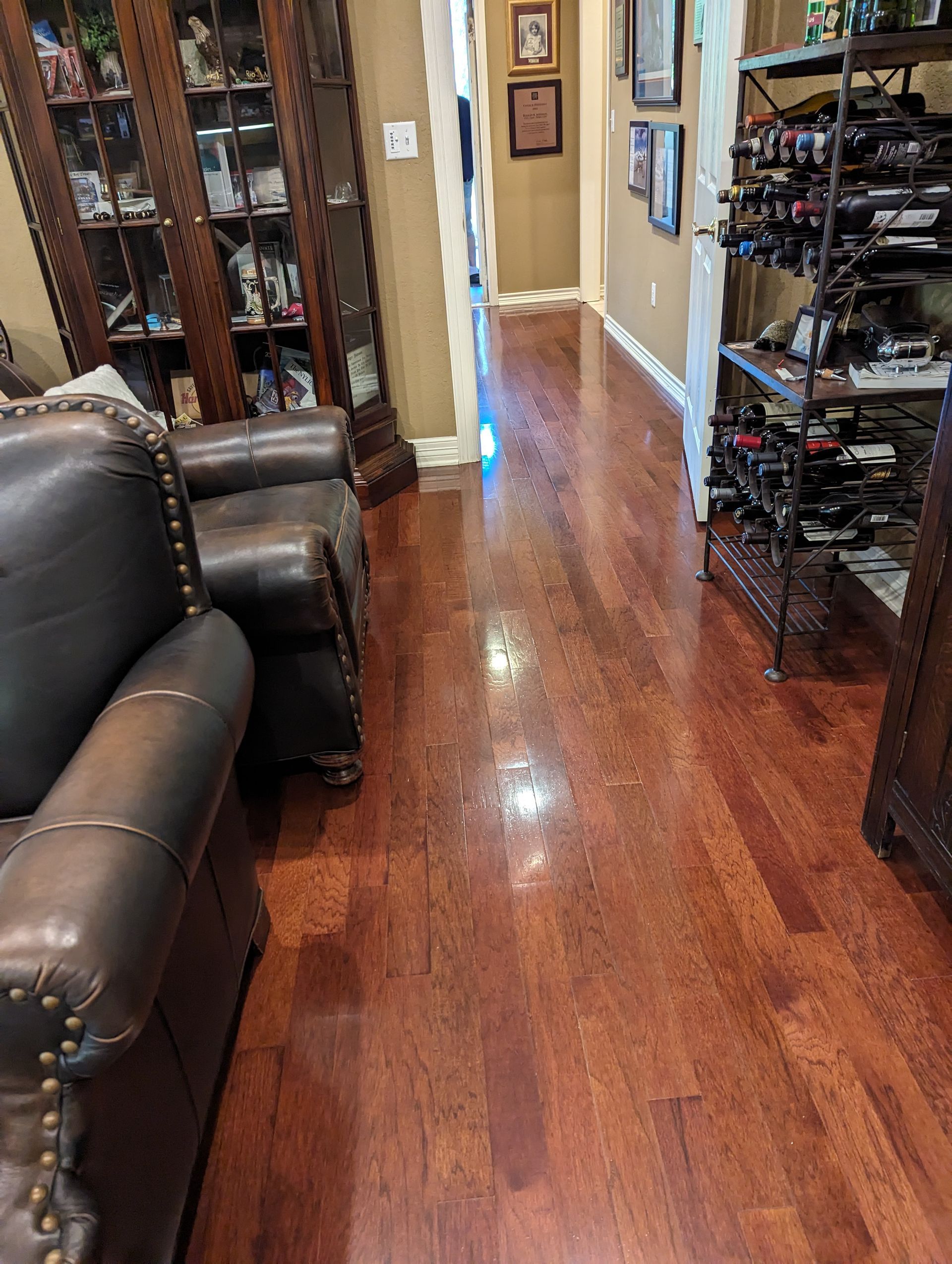 Dark wood floors in a hallway with a leather sofa, wine rack, and a bookcase.