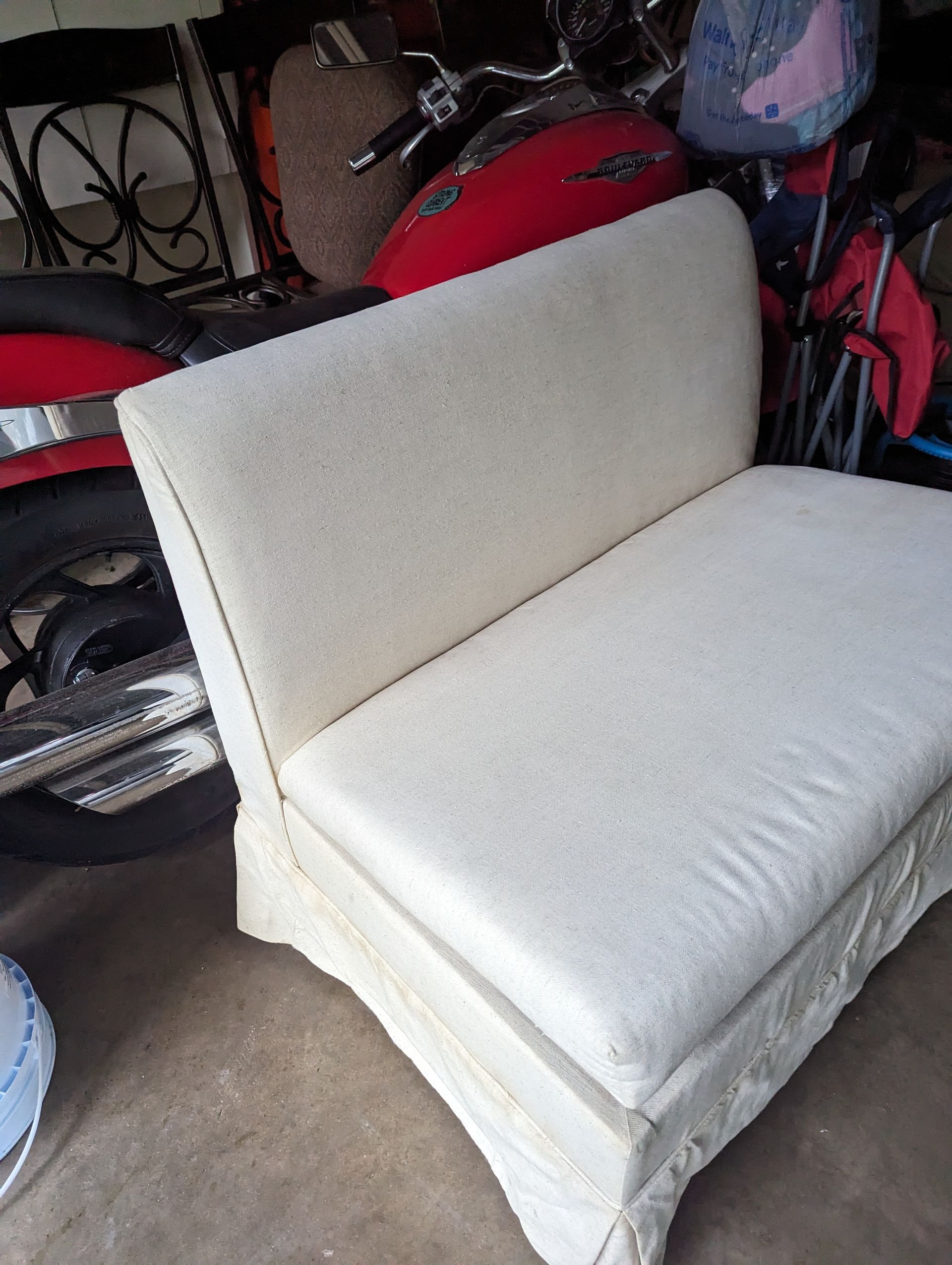 Cream-colored upholstered bench with a curved back, situated near a motorcycle.