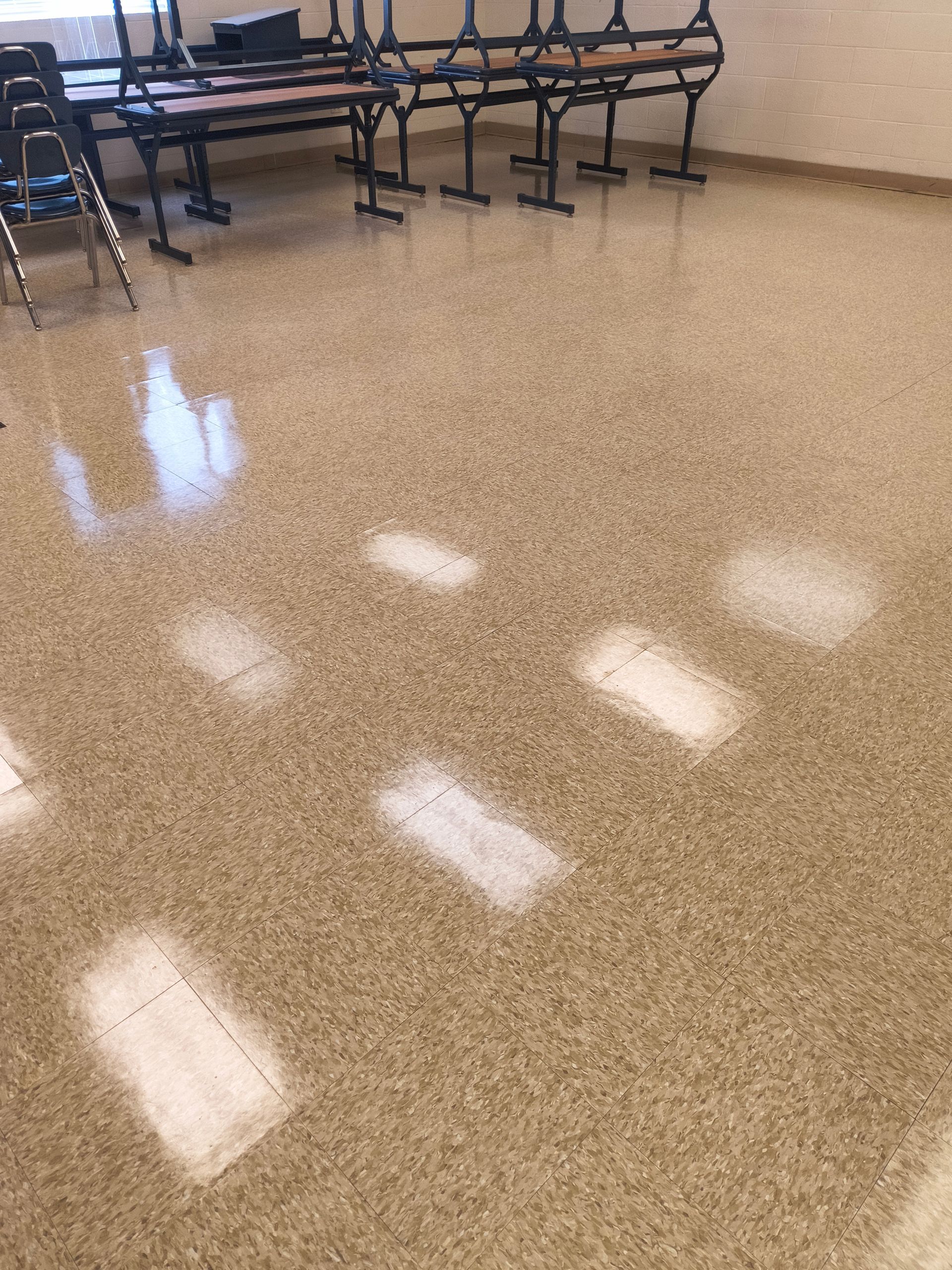 Brown speckled floor with sunlight reflections, tables, and chairs in background.