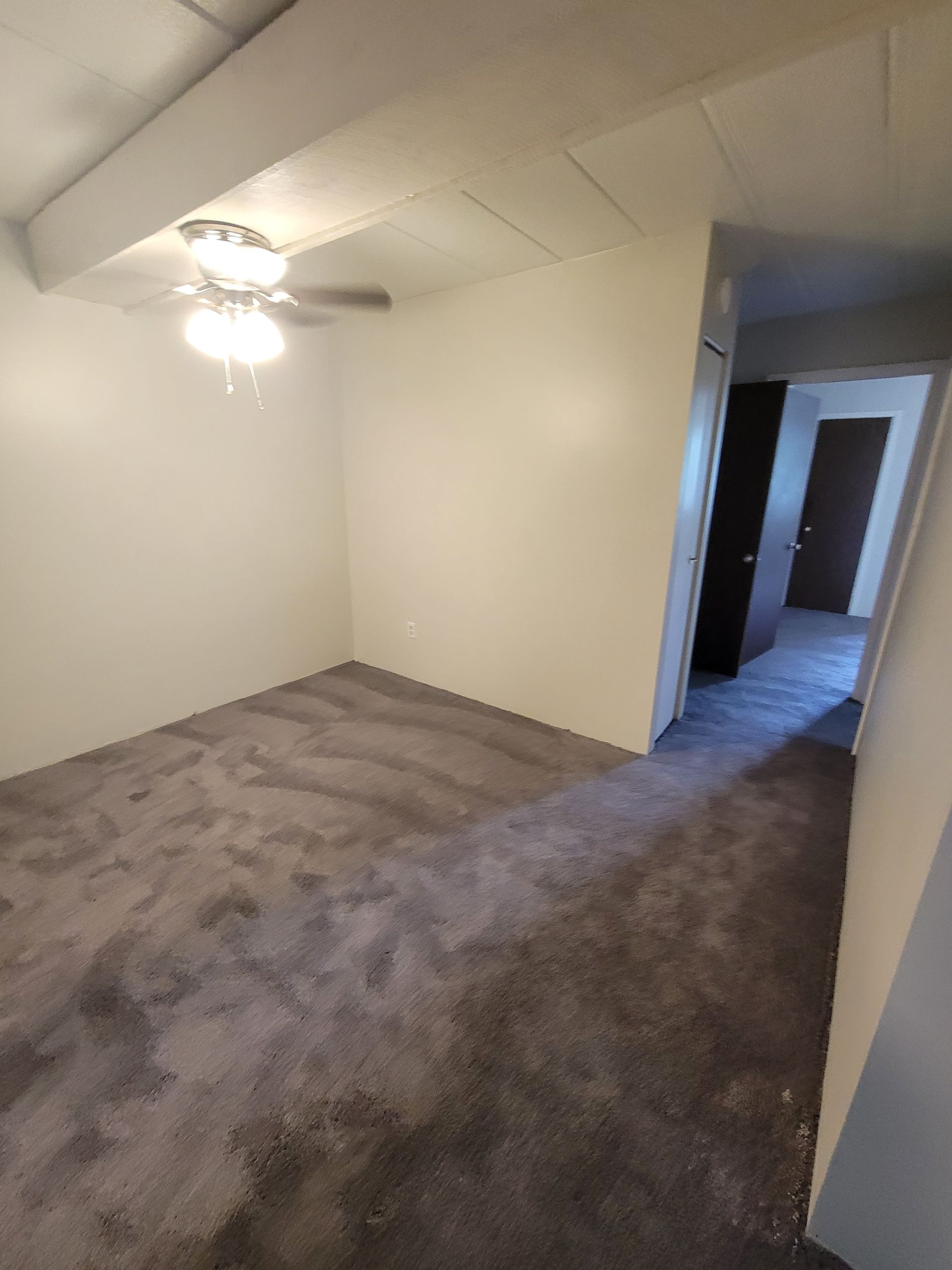An empty bedroom with a ceiling fan and a gray carpet.