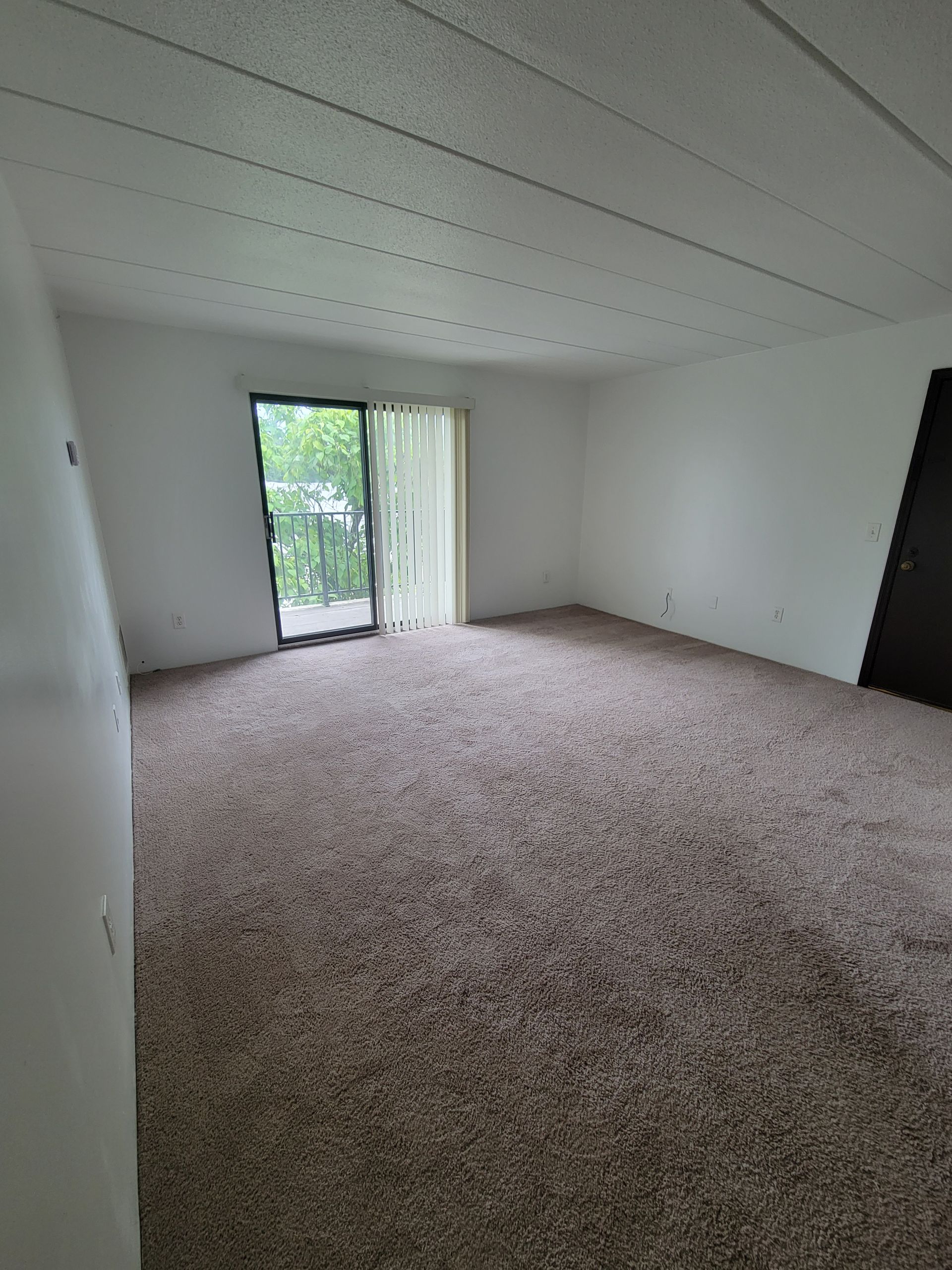 An empty living room with a sliding glass door and a balcony.