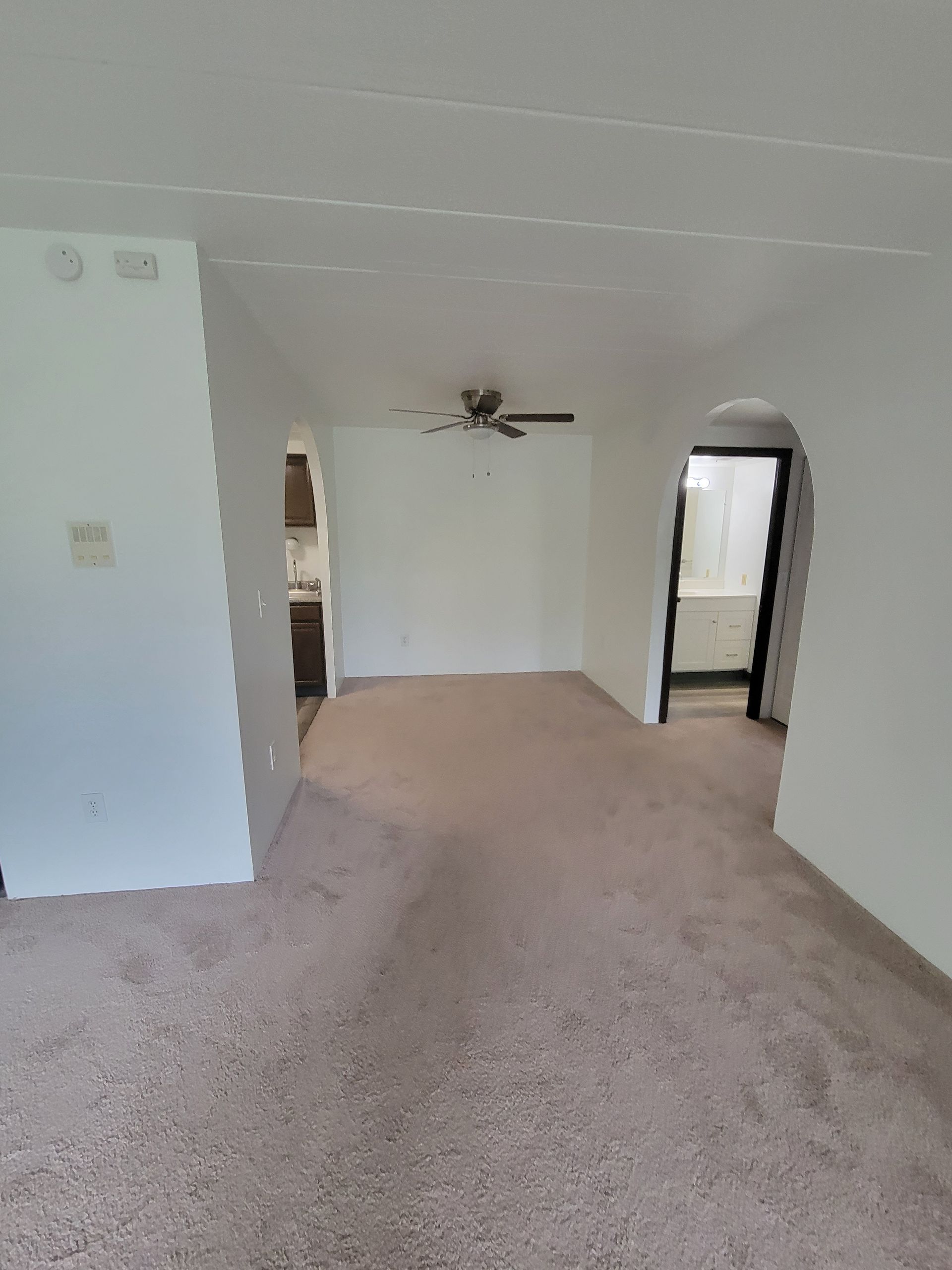 An empty living room with a ceiling fan and a carpeted floor.