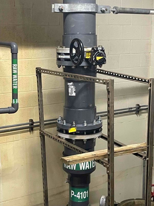 Vertical dark gray PVC pipe with valves, raw water label, and metal support.