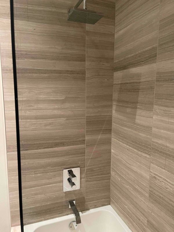 Shower with light brown tiled walls, glass door, and silver fixtures.