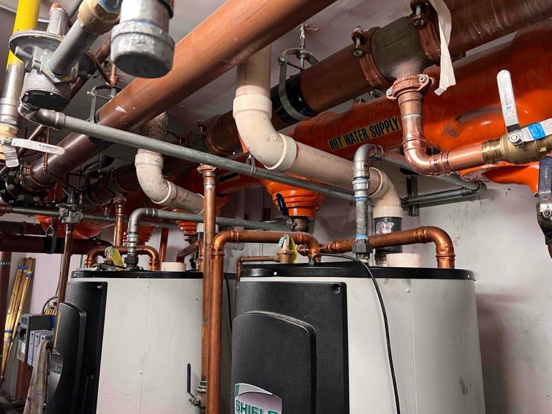 Two cylindrical water heaters with copper pipes and various plumbing in an industrial setting.