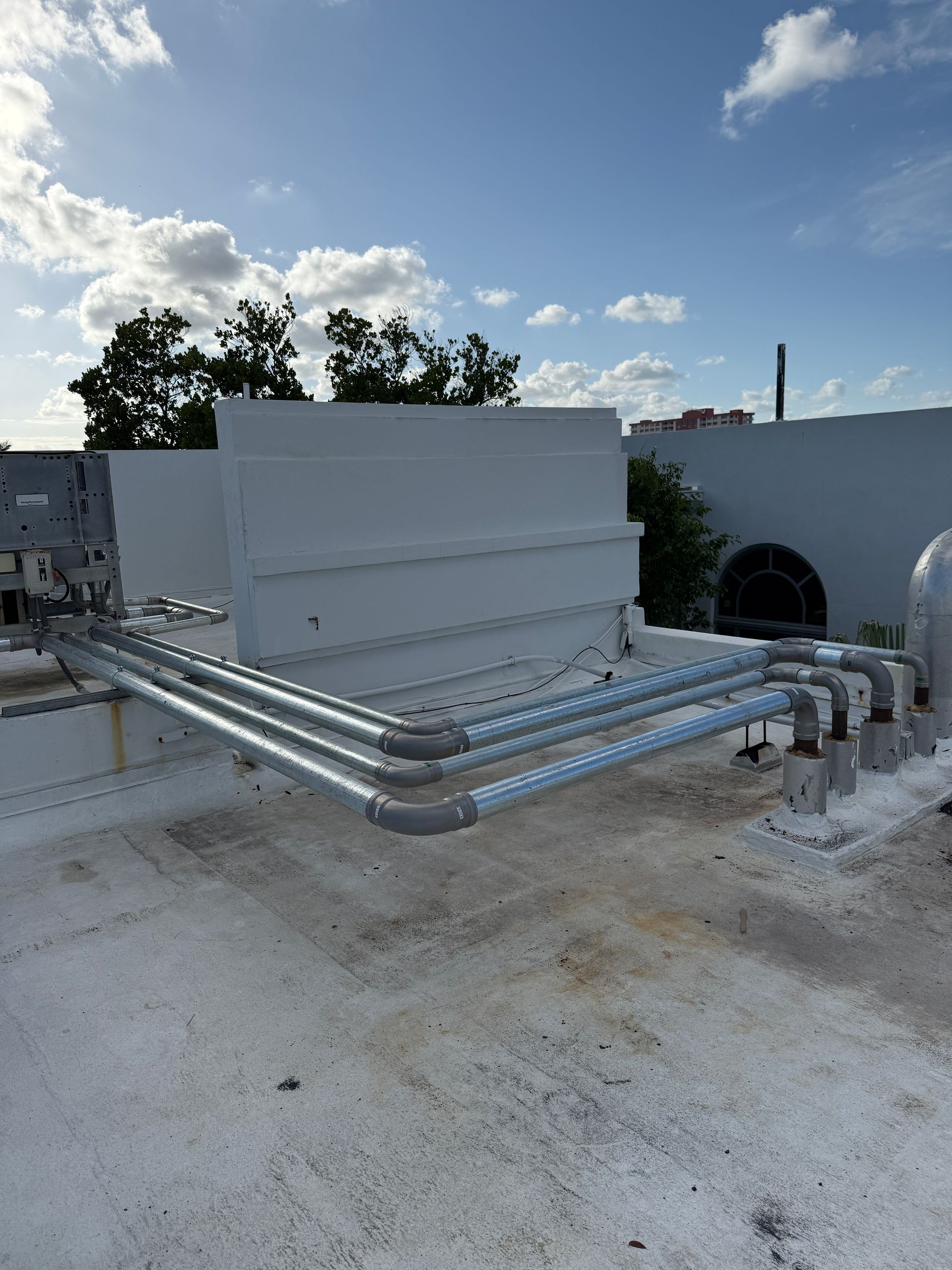 Pipes on a flat roof, leading to a white rectangular structure under a partly cloudy sky.