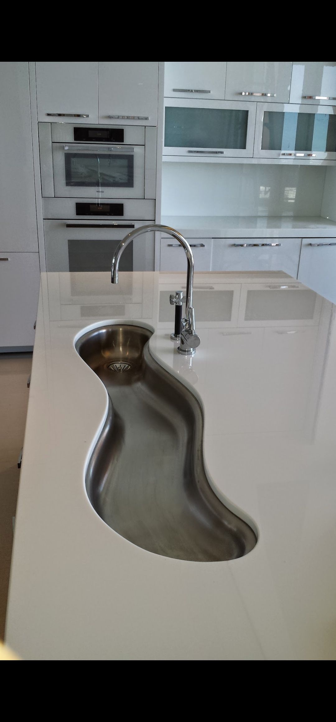A modern kitchen with a unique shaped sink on a white countertop and stainless steel faucet.
