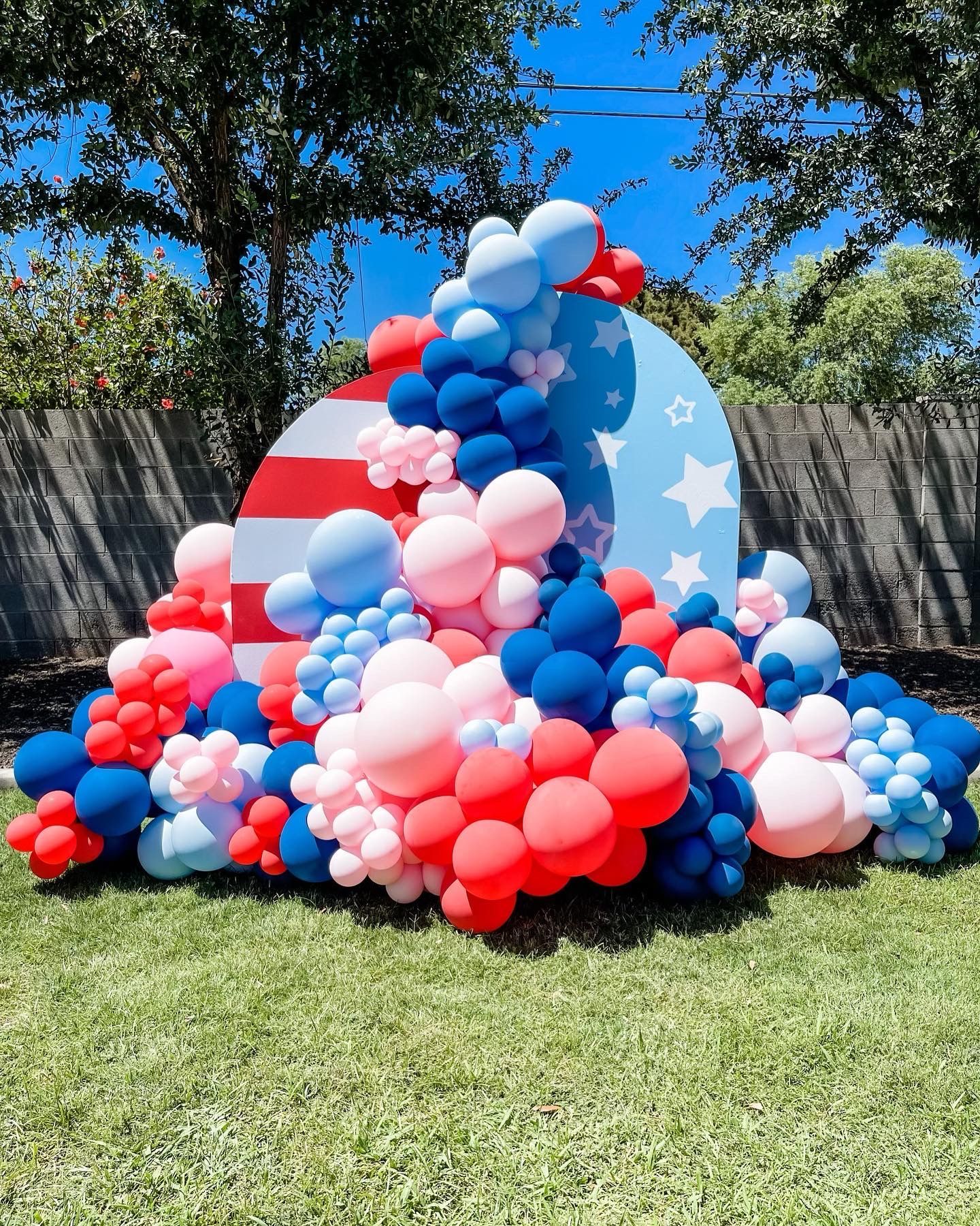 A bunch of red , white , and blue balloons are sitting on top of a lush green field.