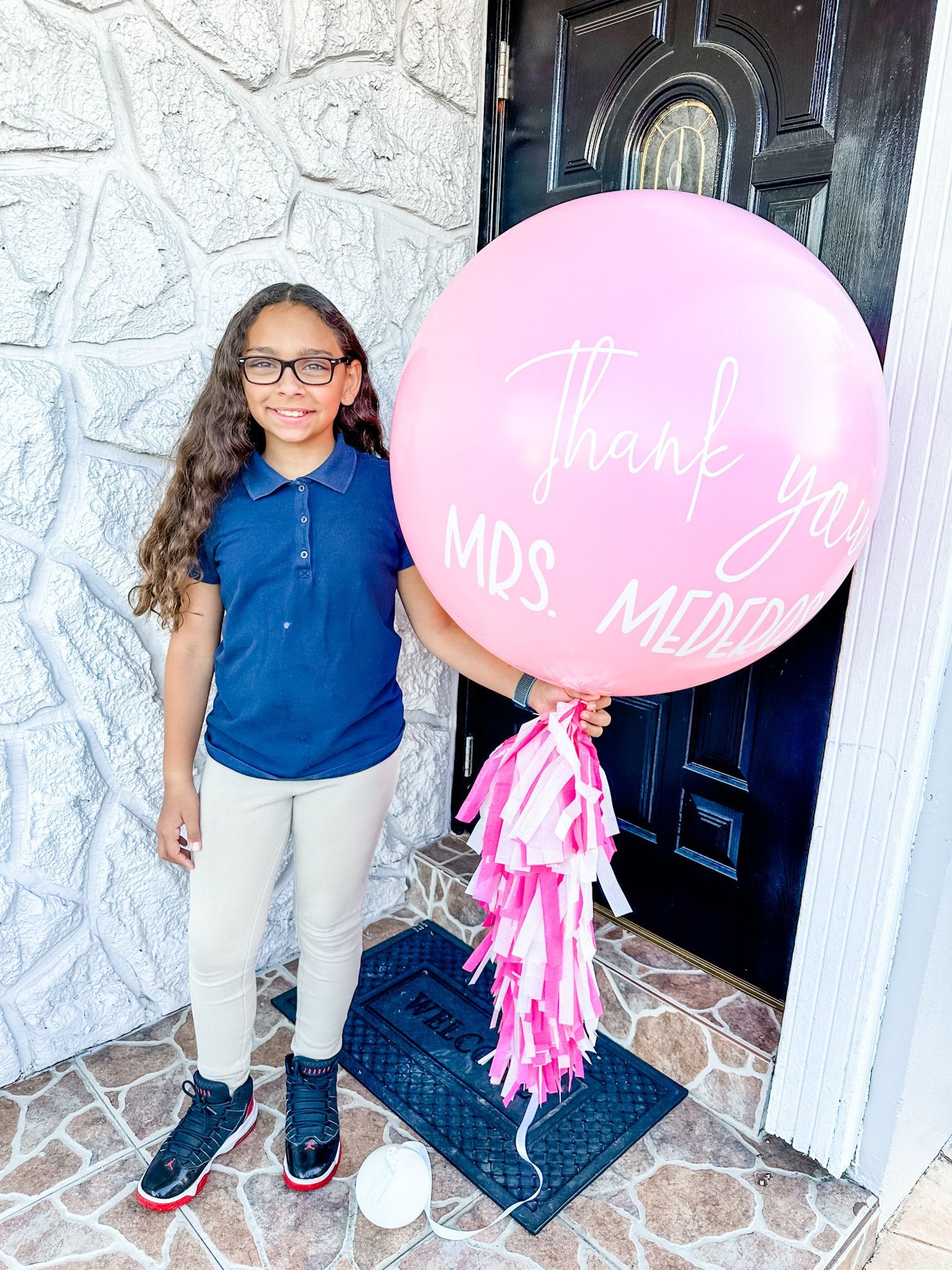 A young girl is holding a large pink balloon in front of a door.