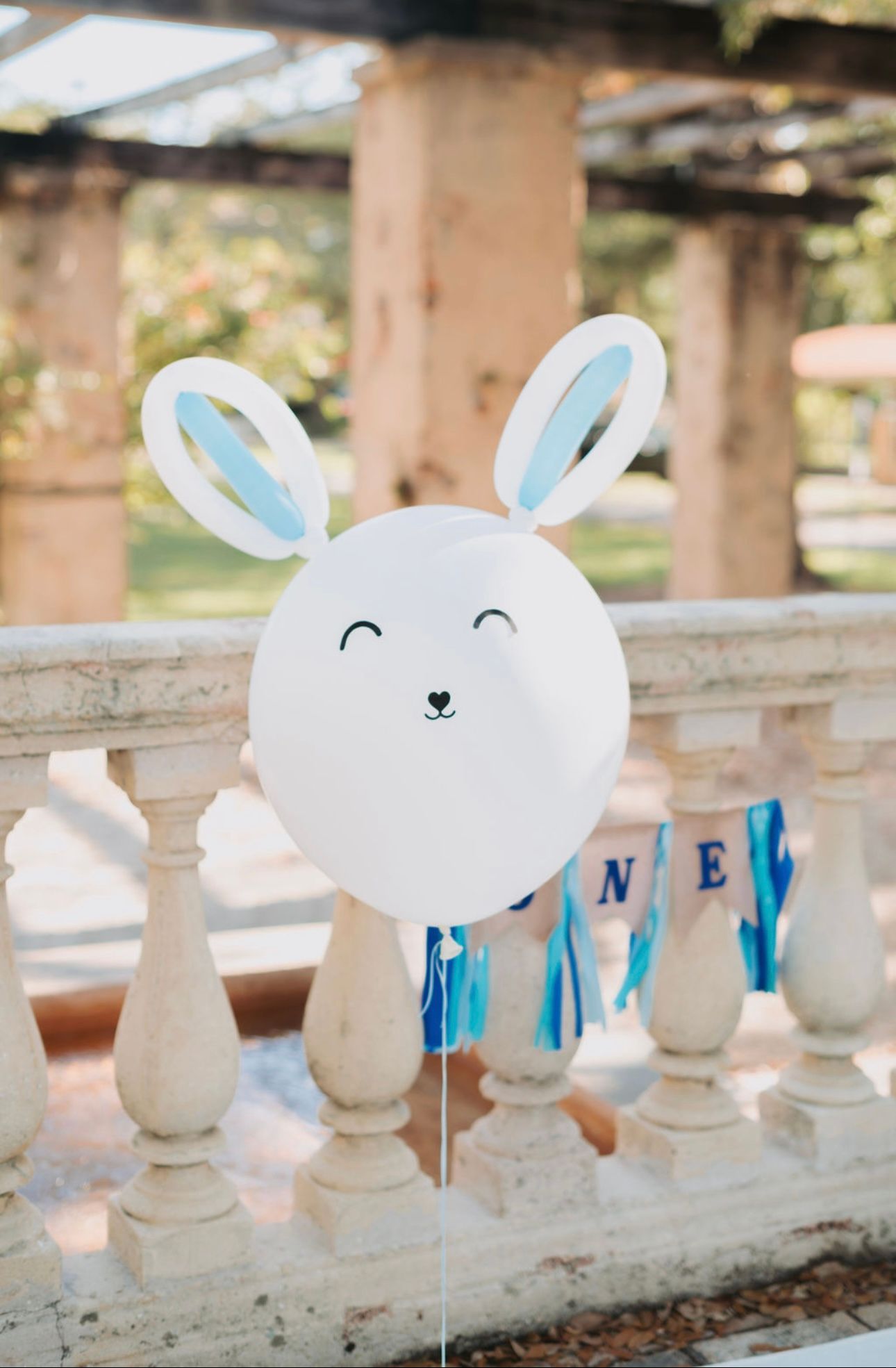 A white balloon with bunny ears is sitting on a railing.