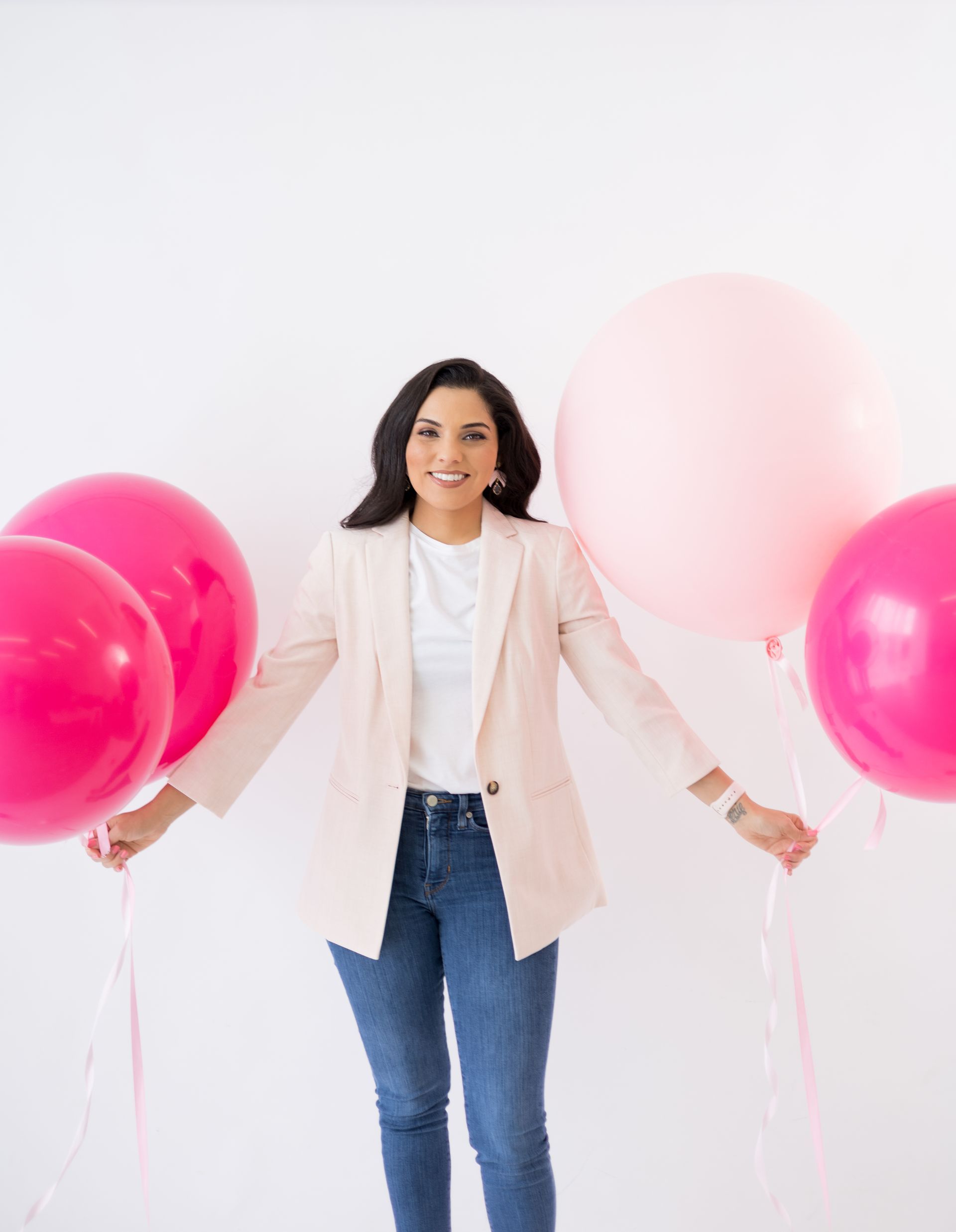 A woman in a white jacket is holding pink balloons.