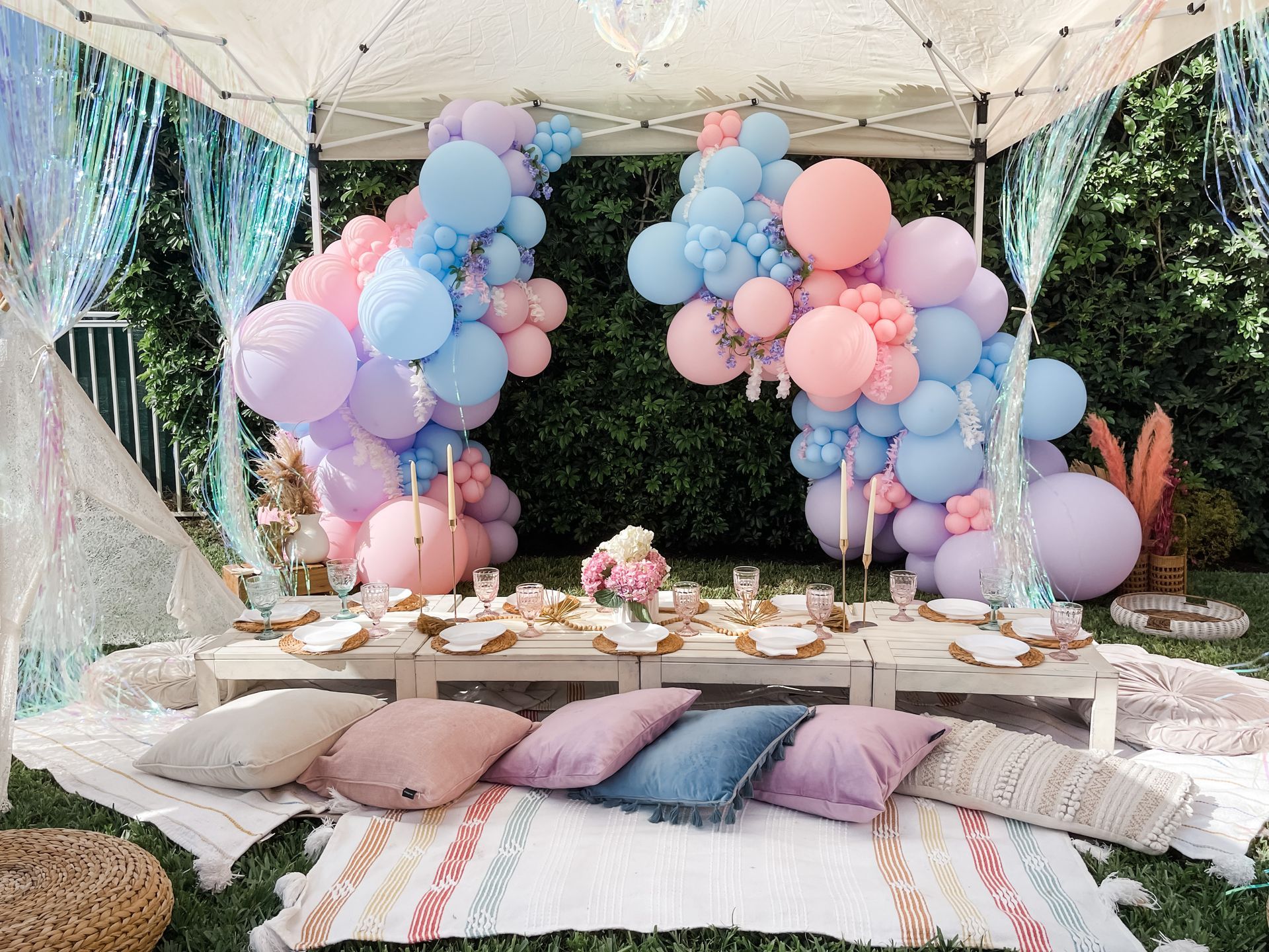 A picnic table with balloons and pillows under a tent.