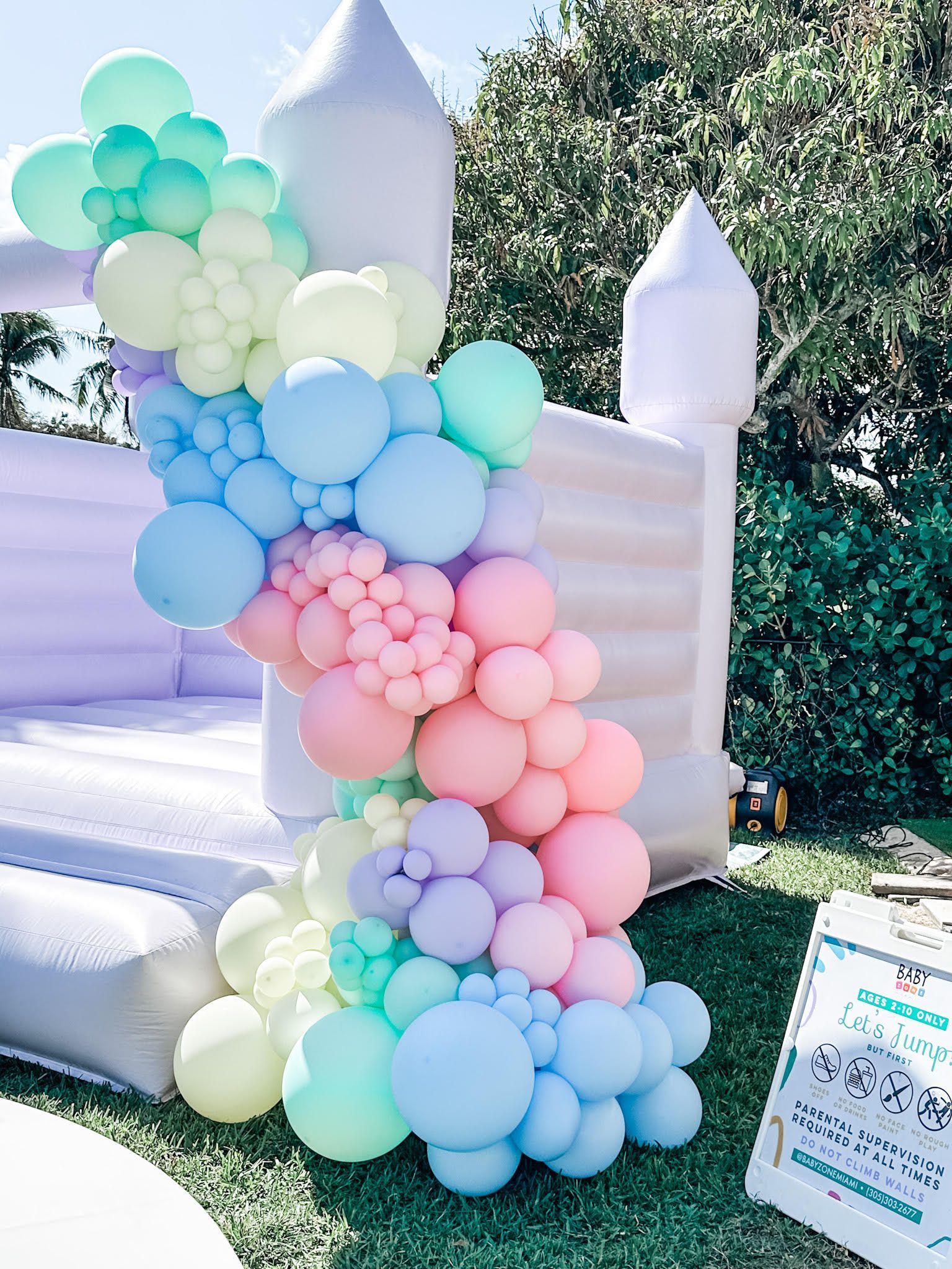 A bunch of balloons are sitting in front of a bouncy castle.