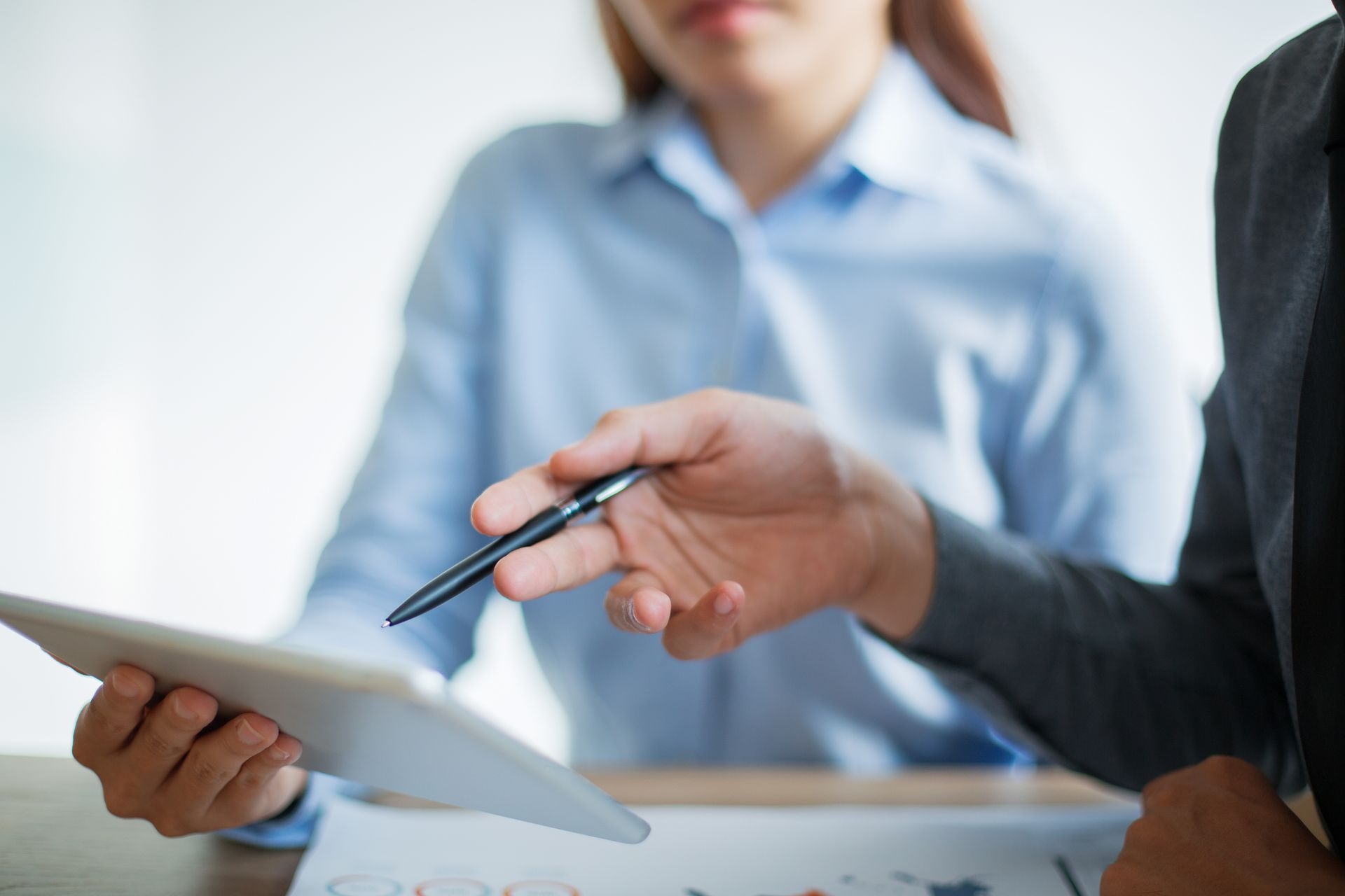Scheduling a consultative review of your financial return potential. A close-up of two professionals collaborating at a desk, with one person using a pen to point at specific data points on a digital tablet held by the other, symbolizing a detailed consultative review of insurance performance.